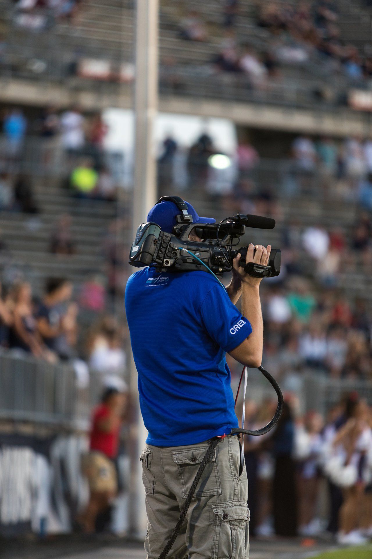 Camera operator in blue shirt filming a stadium event from the sidelines