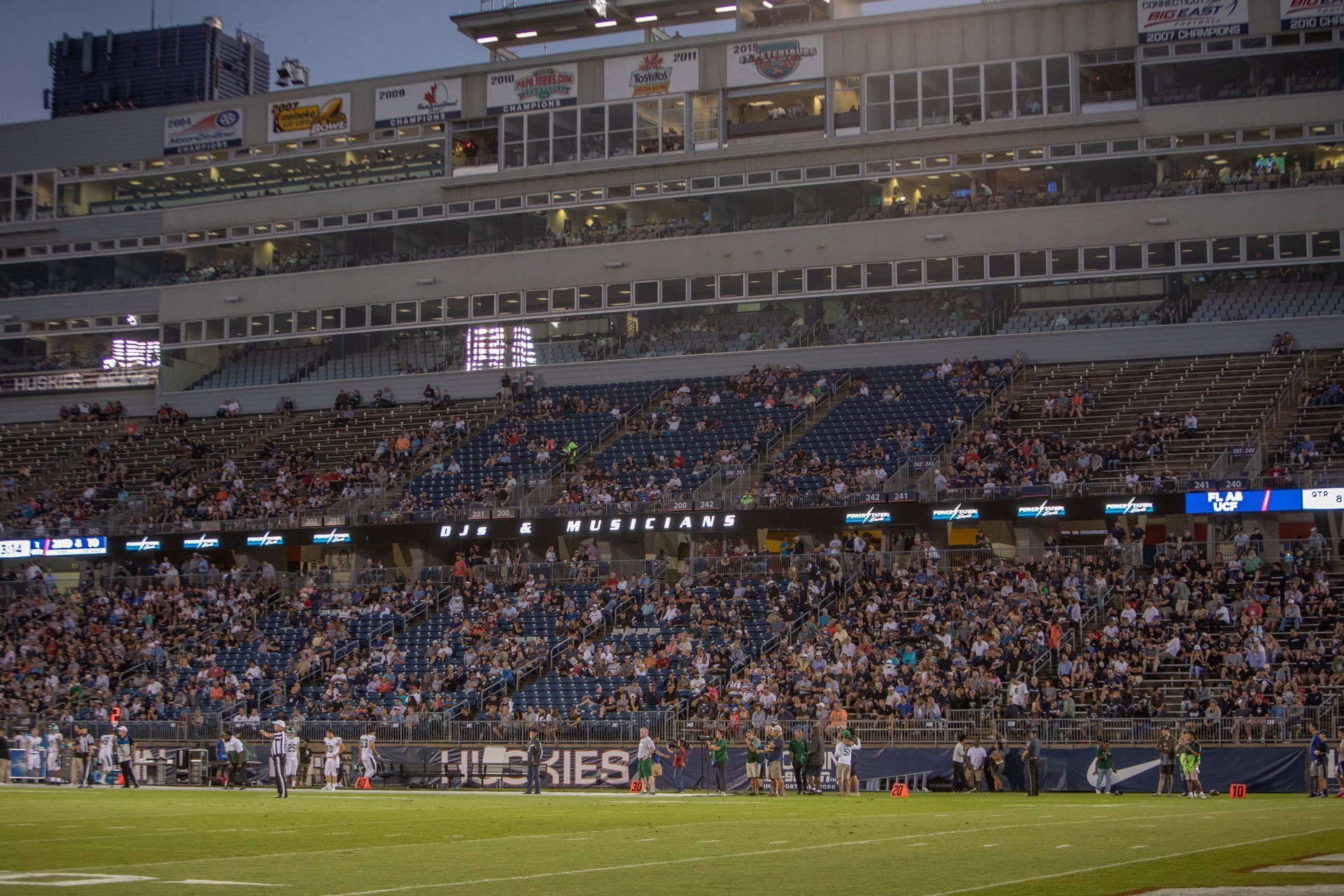Packed baseball stadium at dusk, with a crowd in the stands and players on the field.