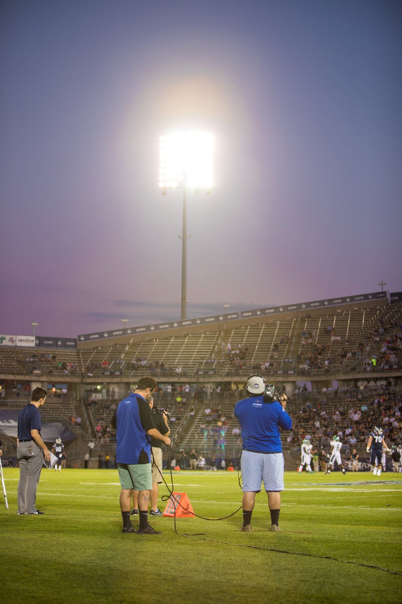 Soccer stadium at night with bright floodlights, players and staff on the field, and a packed crowd in the stands
