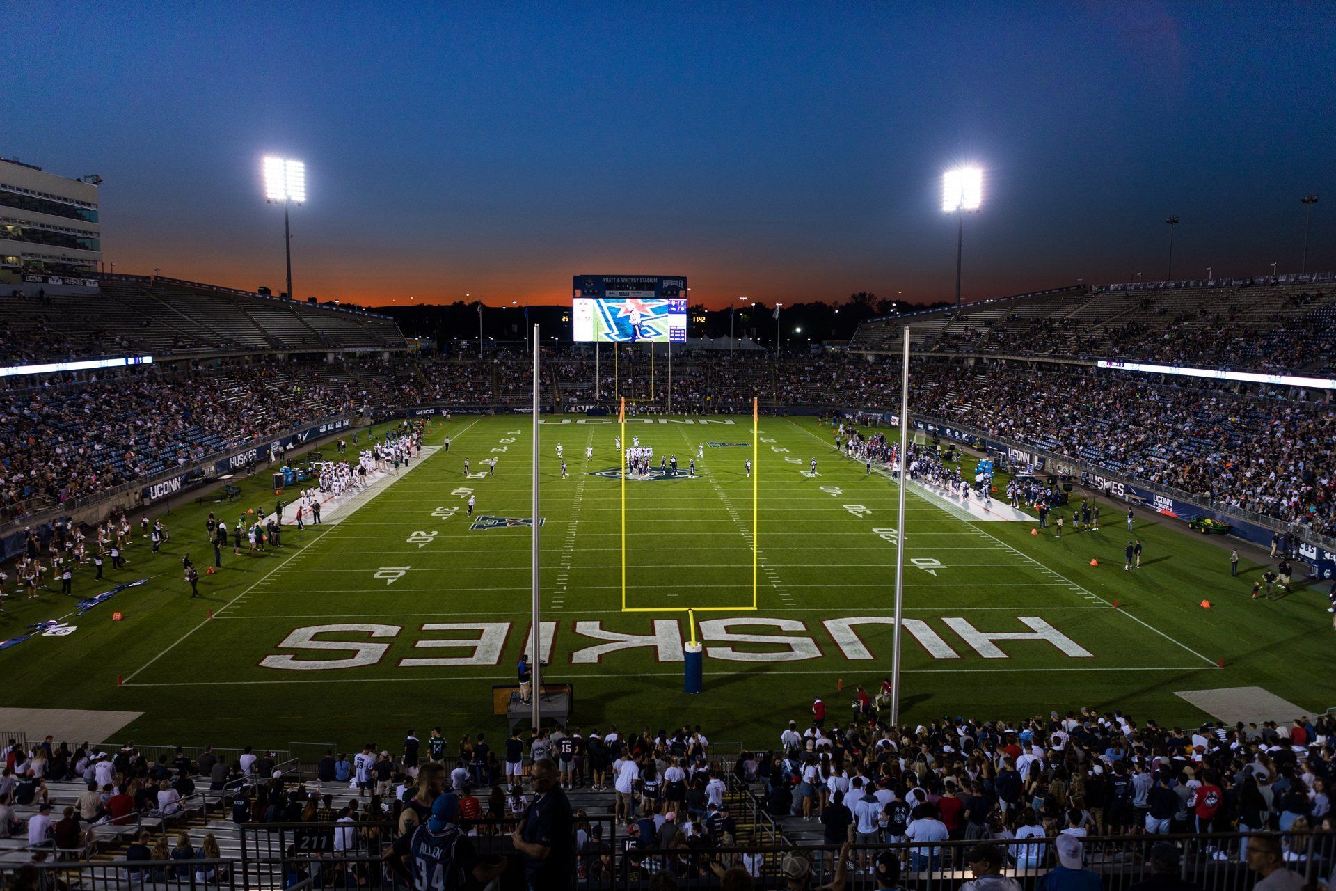 Nighttime football stadium packed with fans, brightly lit field, and “KANSAS” painted in the end zone.