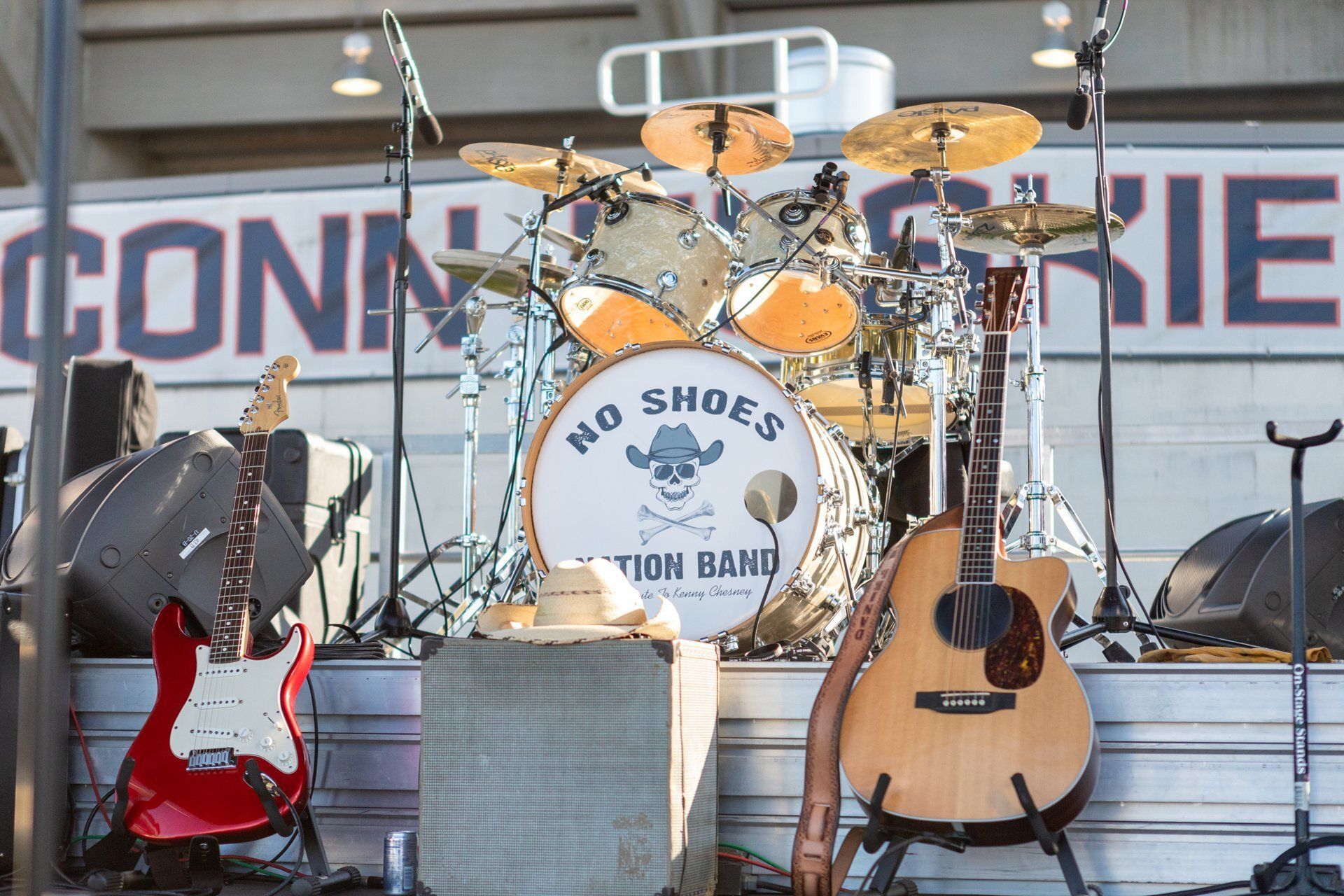 Empty band stage with drum kit, red electric guitar, acoustic guitar, and microphone stands on risers.