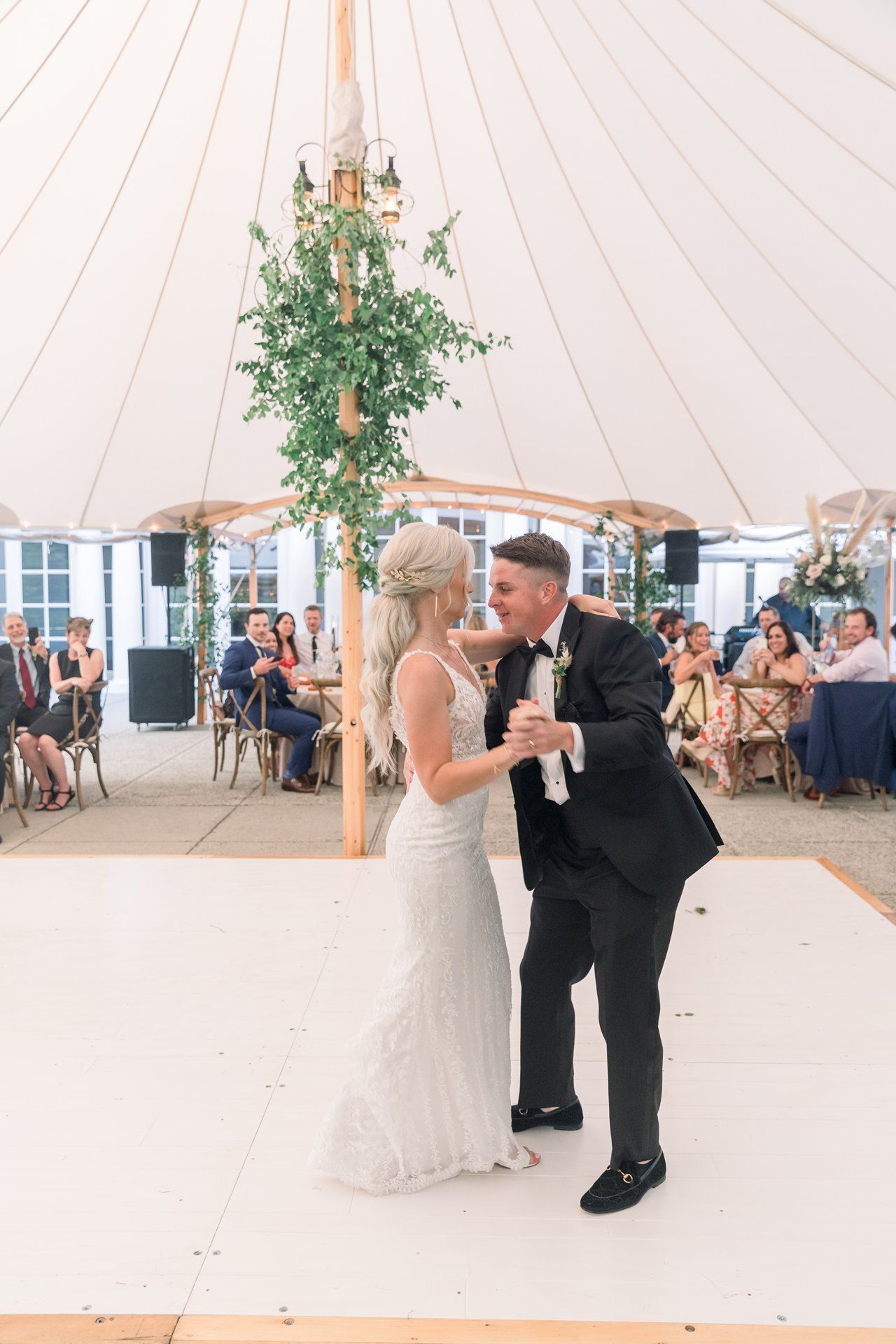 Bride and groom dancing beneath a tent with hanging greenery at a wedding reception