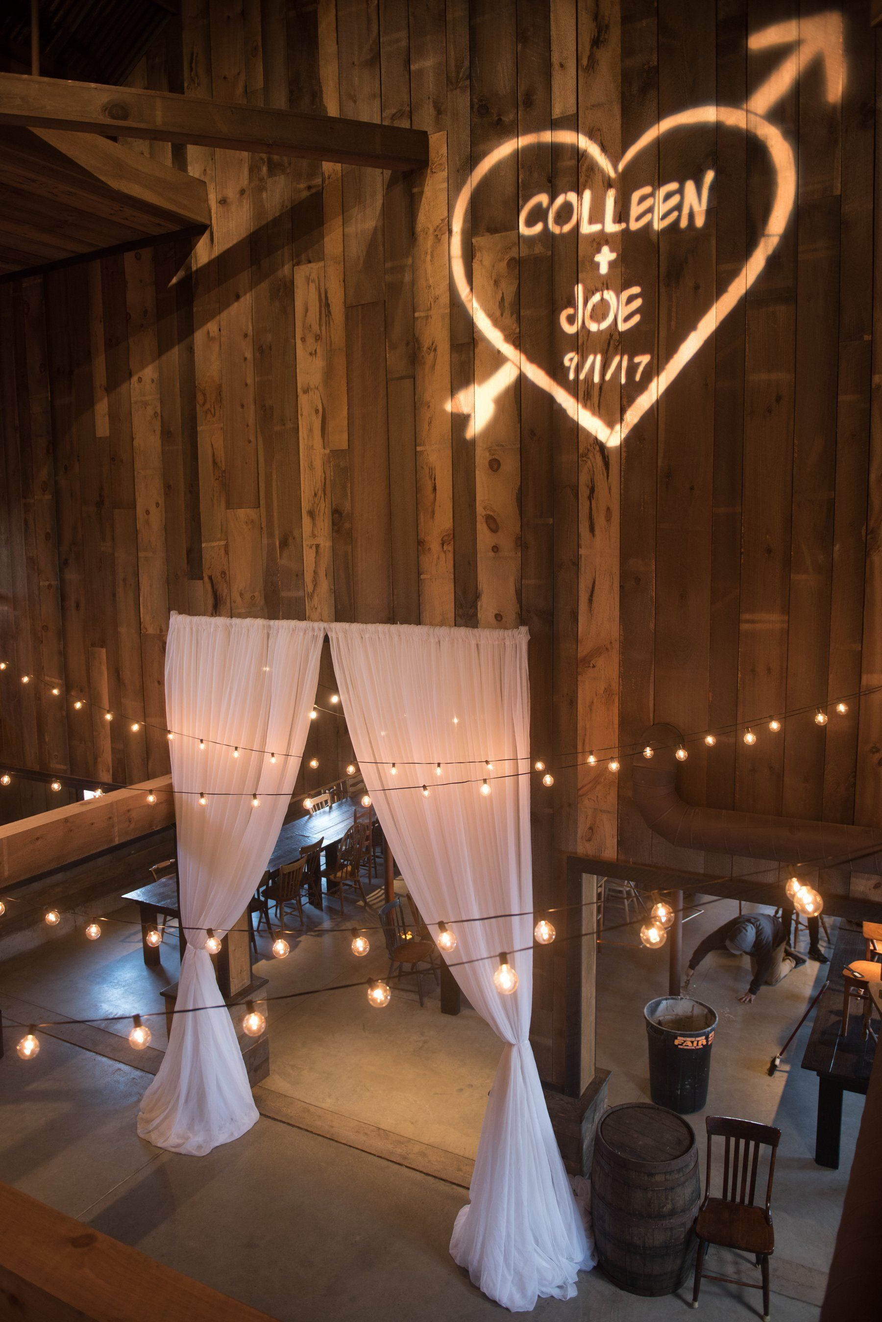 Wedding reception with heart-shaped neon sign and draped photo backdrop in a rustic barn