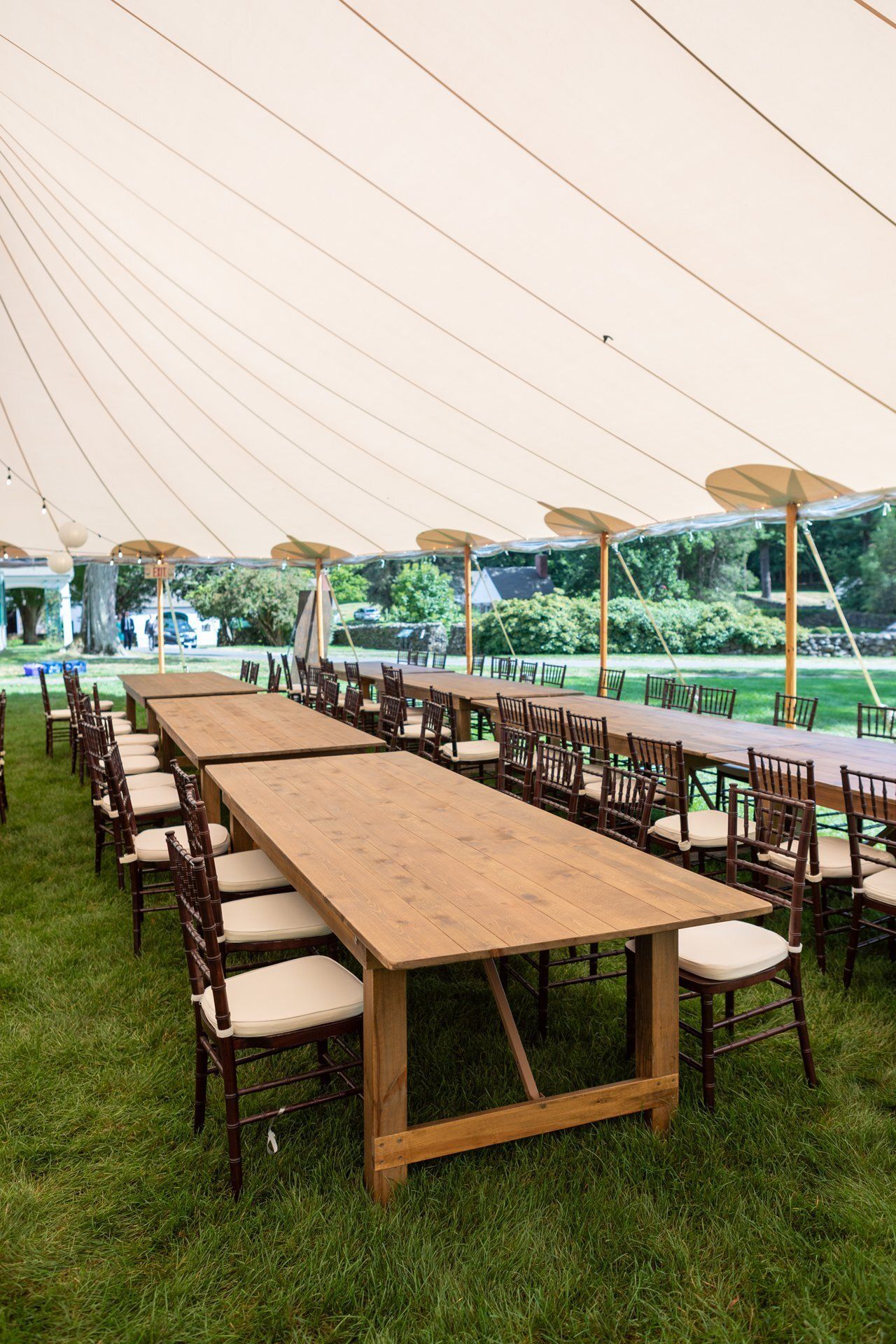 Rows of wooden picnic tables under a large white canopy on a grassy lawn outdoors