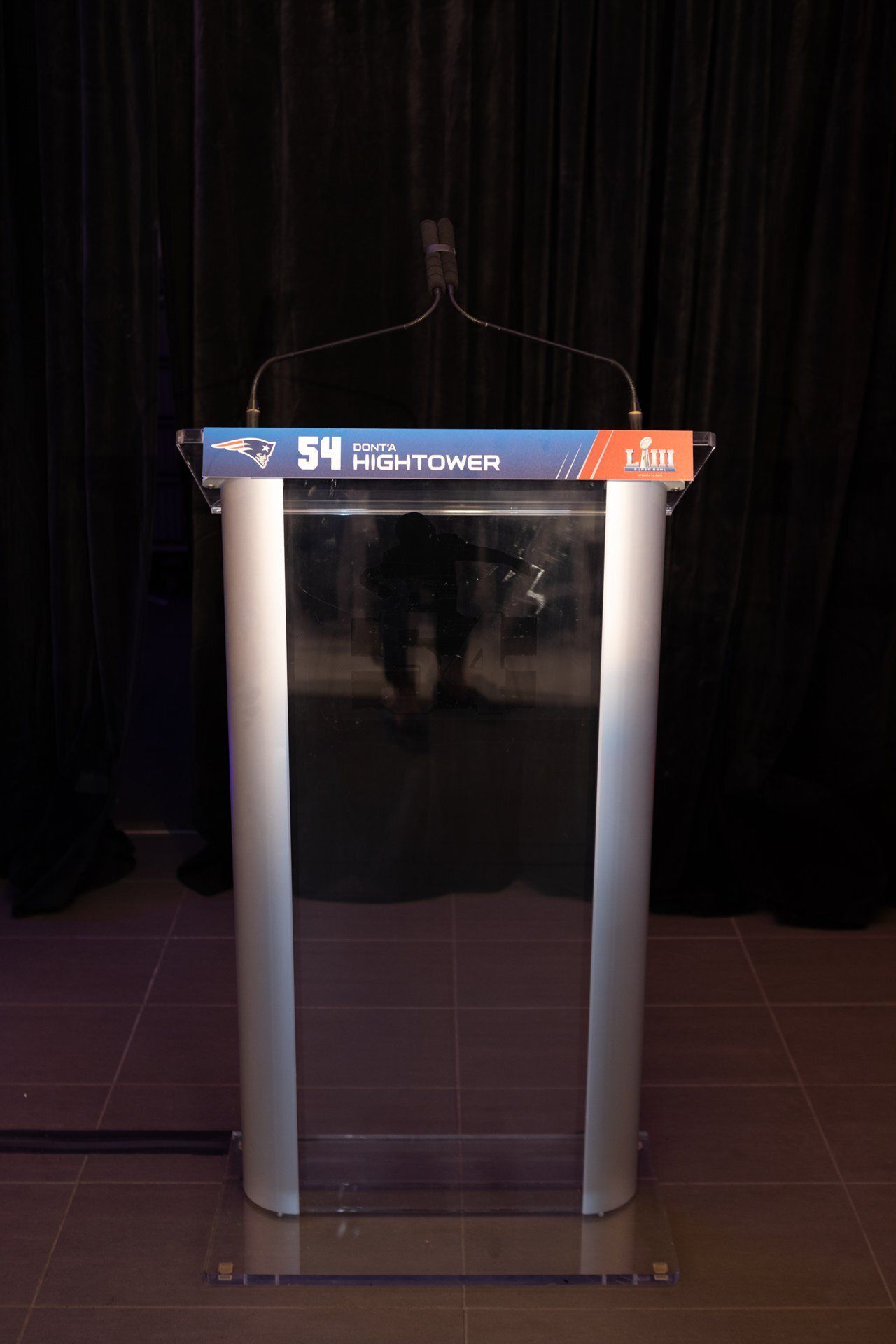 A clear acrylic podium with two white columns and a dark top, centered on a stage with black curtains.