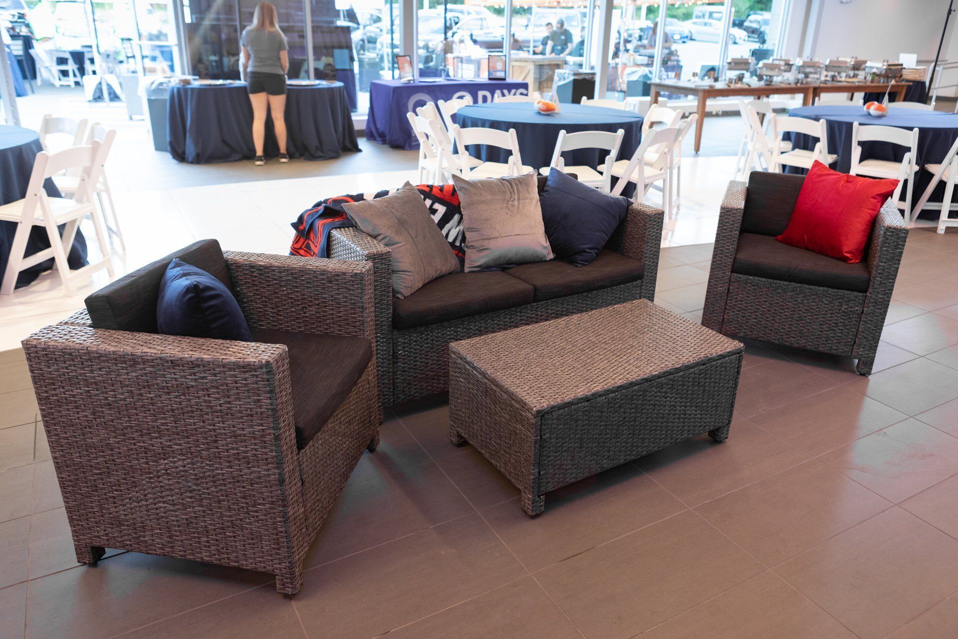 Wicker patio sofa set with dark cushions and red accent pillows in an outdoor dining area