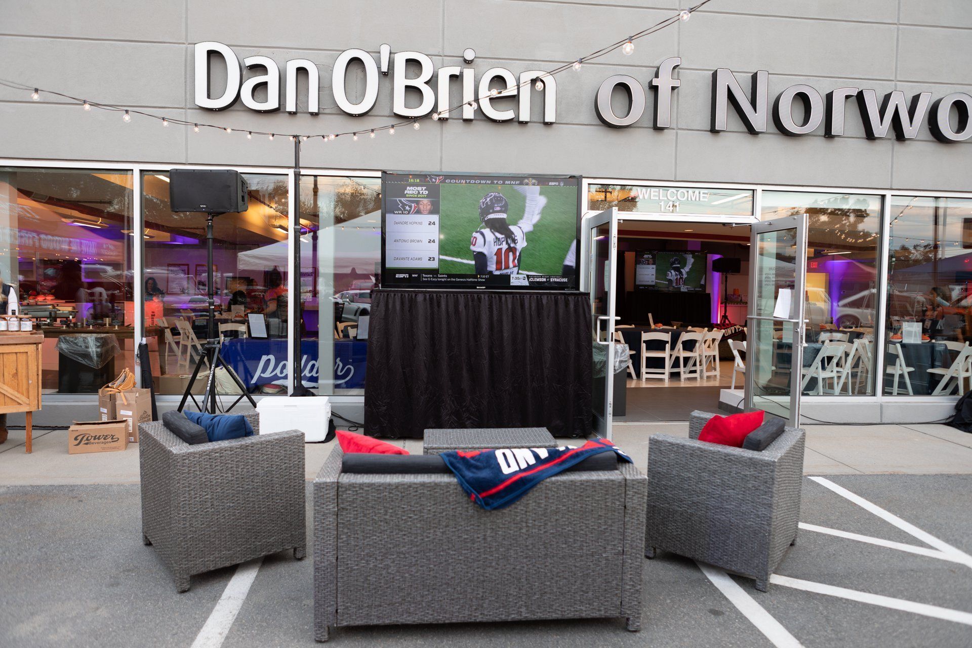 Outdoor lounge with gray chairs and red-blue blankets in front of Dan O'Brien on Norwood dealership window