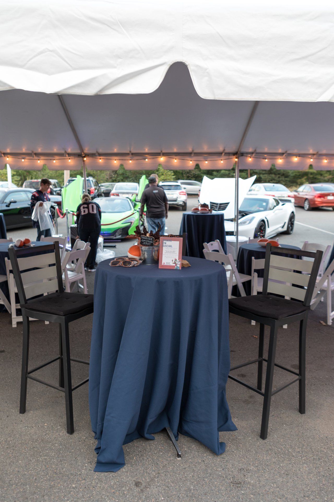 Covered outdoor event table with blue tablecloth, folded chairs, and cars parked behind it at dusk