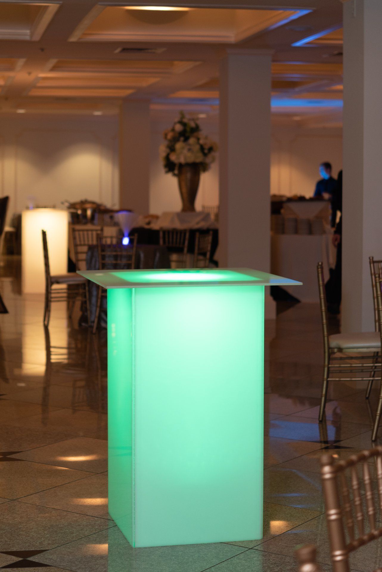 Glowing green cocktail table in a softly lit banquet hall with empty chairs nearby