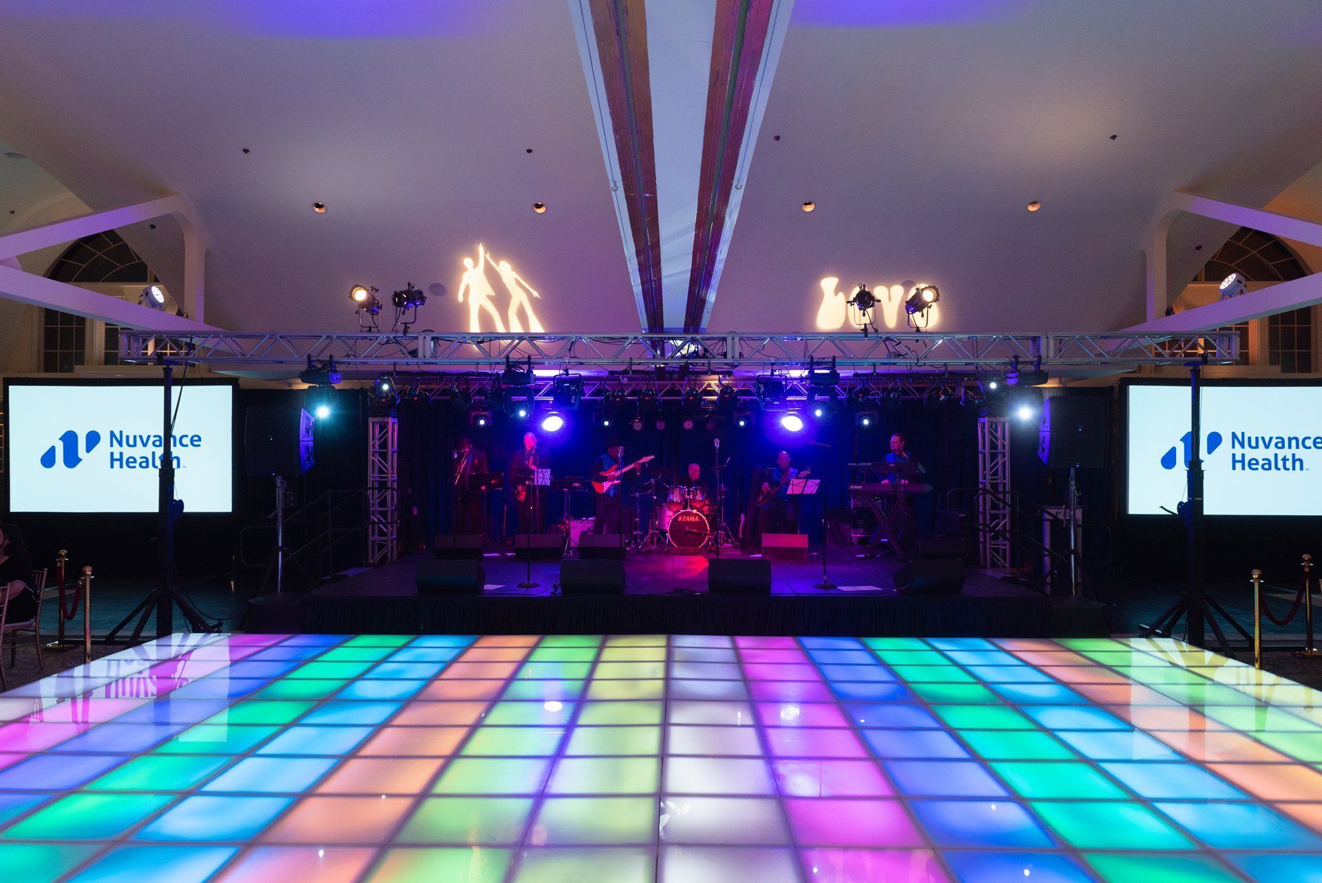 Colorful lit dance floor in a banquet hall with a stage and screens in the background
