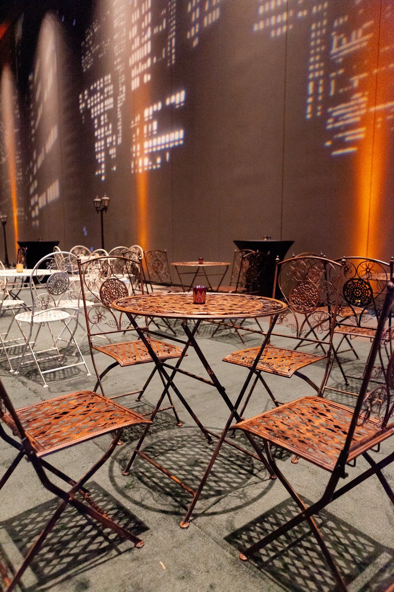 Outdoor café seating with small black tables and folding chairs against a warm, textured wall