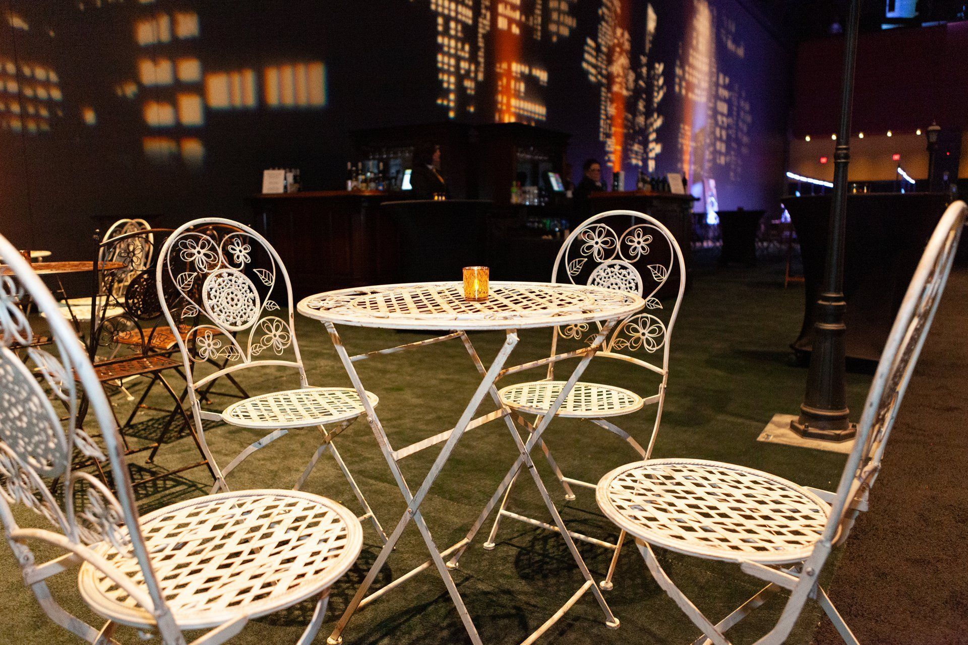 White wrought-iron café table and chairs on a patio at night with city lights in the background