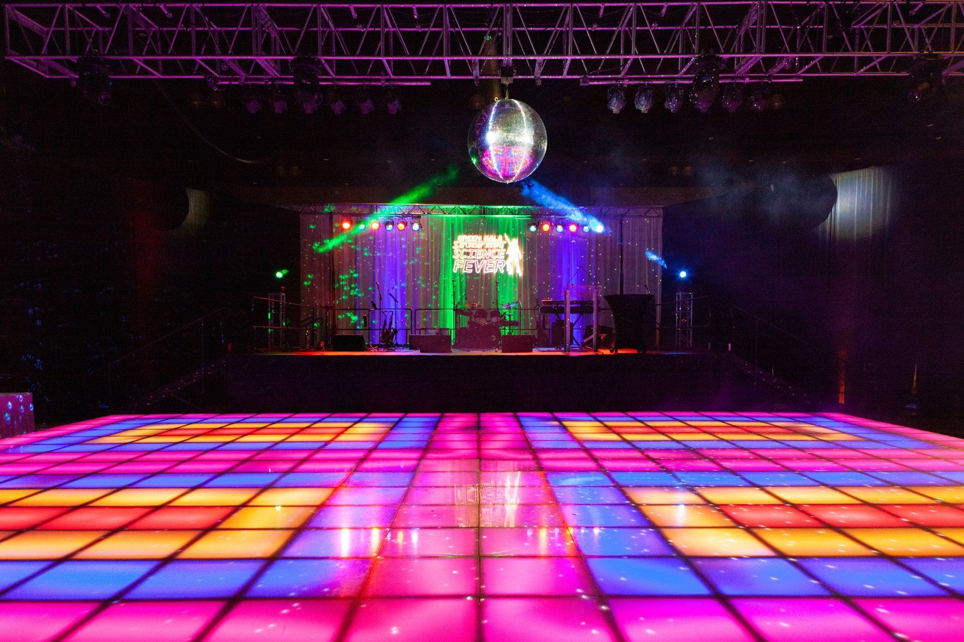 Colorful lit dance floor with a disco ball and neon lights in a dark club venue