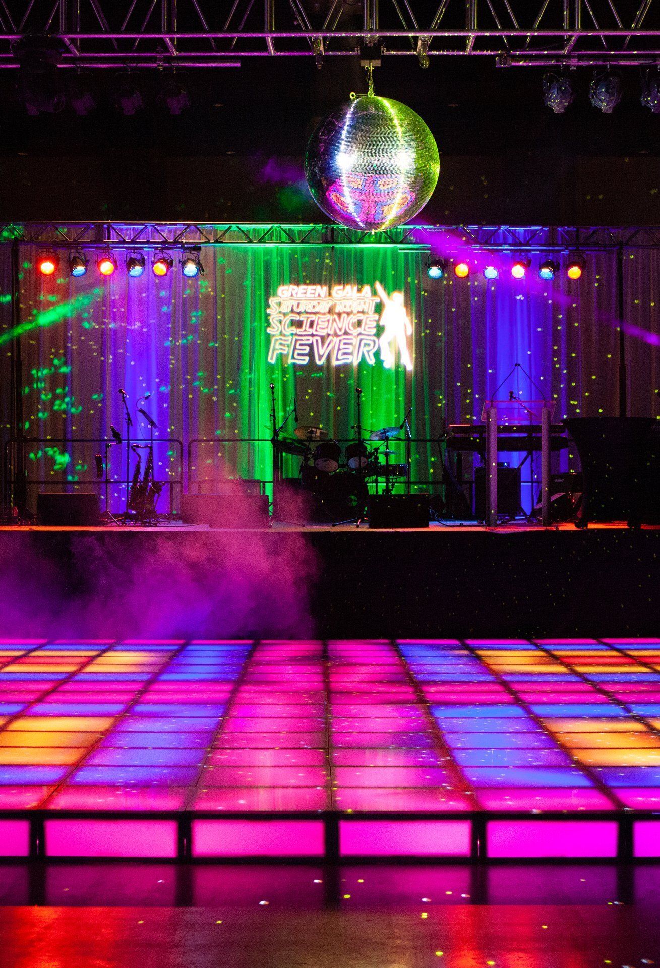 Colorful disco dance floor under a mirrored ball in a nightclub with stage lights and fog