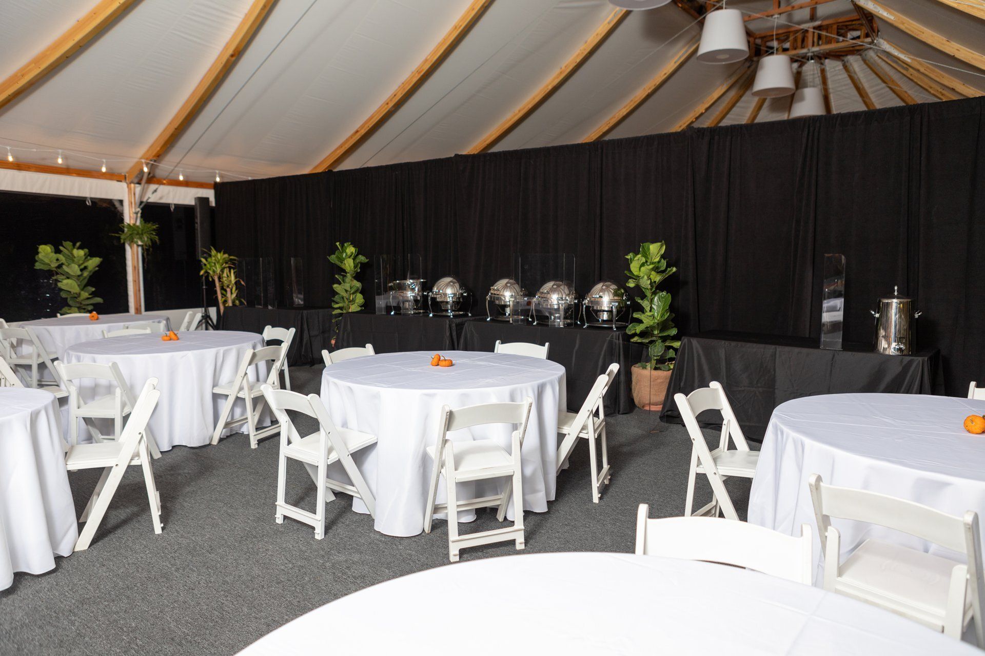 Empty event tent with round tables and white chairs set up on a black carpet floor.