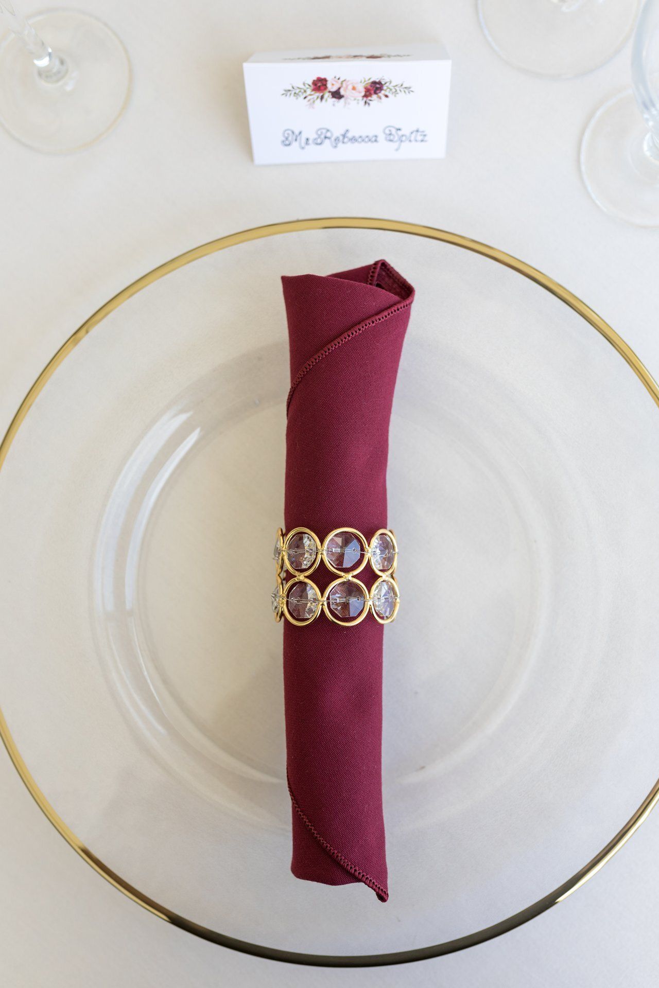 Burgundy cloth napkin with gold ring on white plate with gold rim.