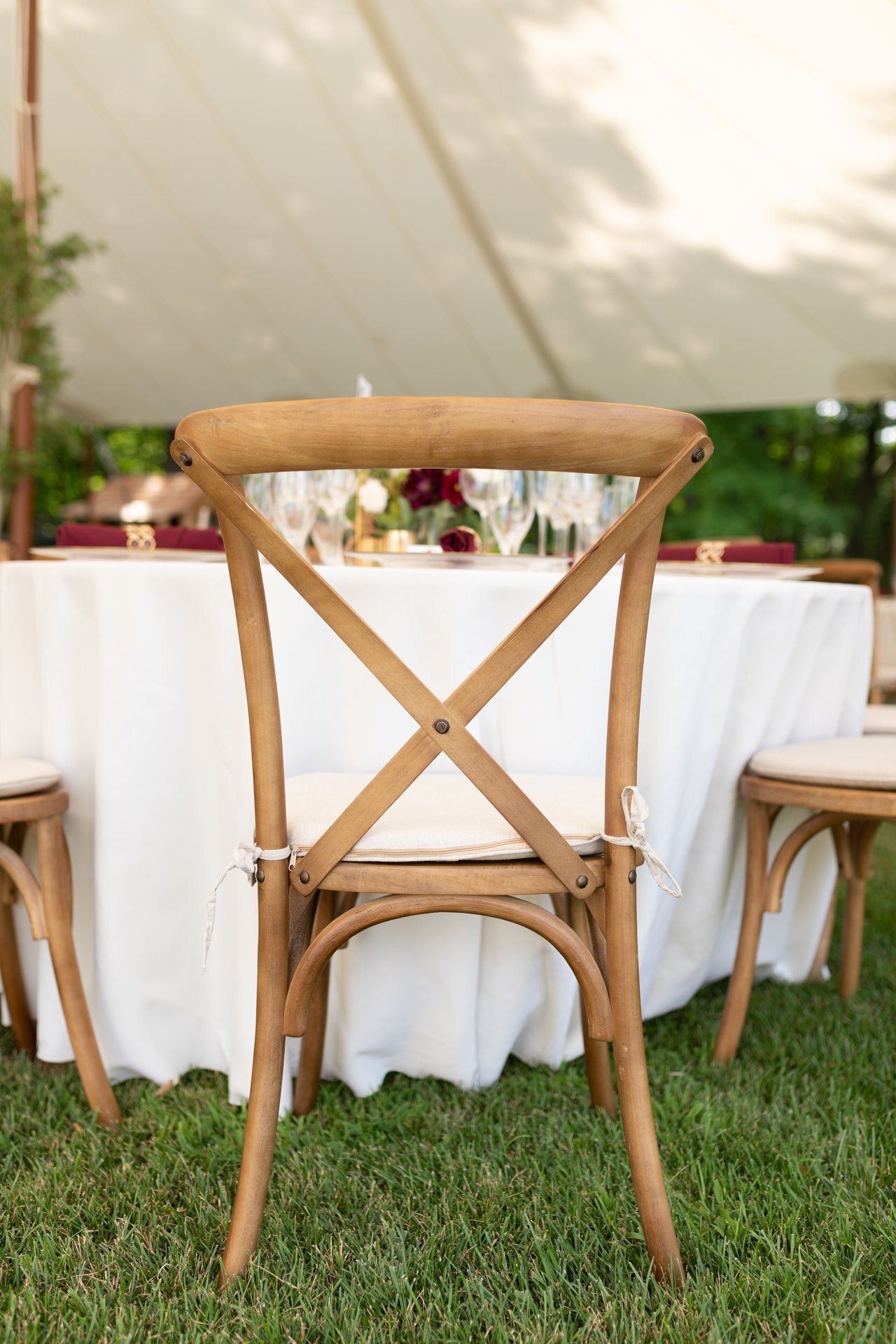 Wooden chair in front of a round white-draped table at an outdoor event on grass