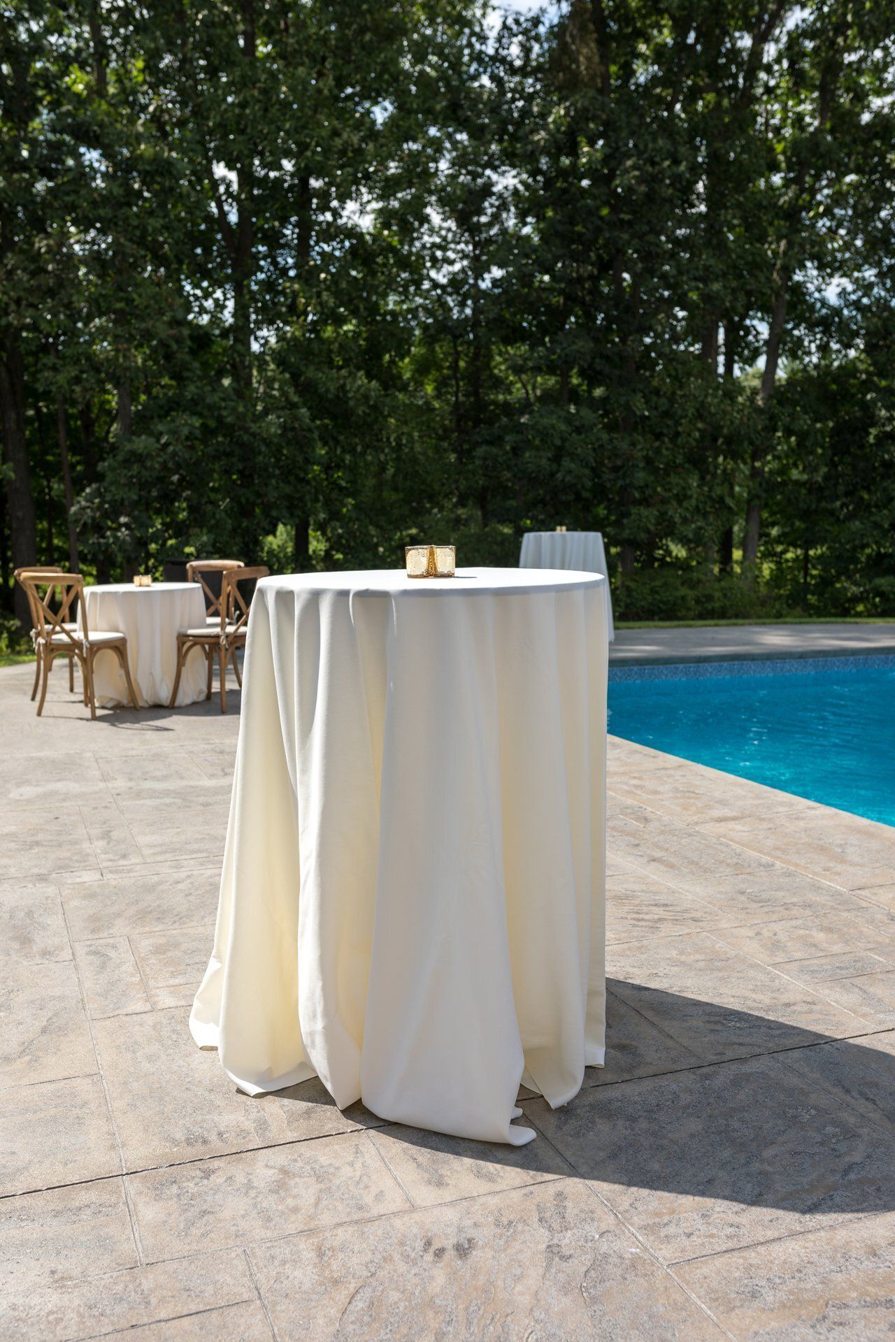 Cocktail table draped in white linen beside a blue pool on a sunlit patio