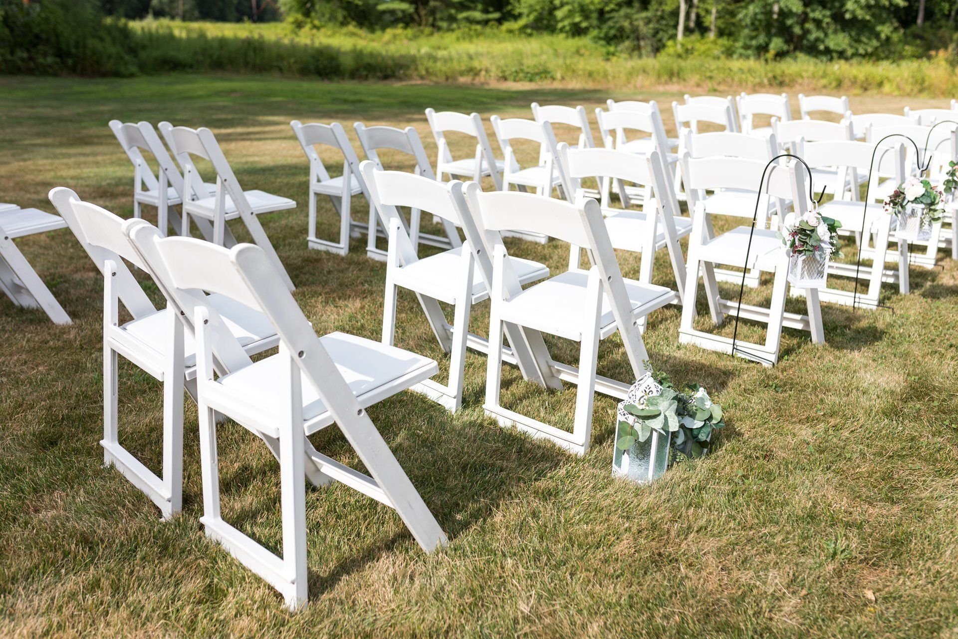 White folding chairs arranged on a grassy lawn for an outdoor ceremony, with floral aisle decorations.