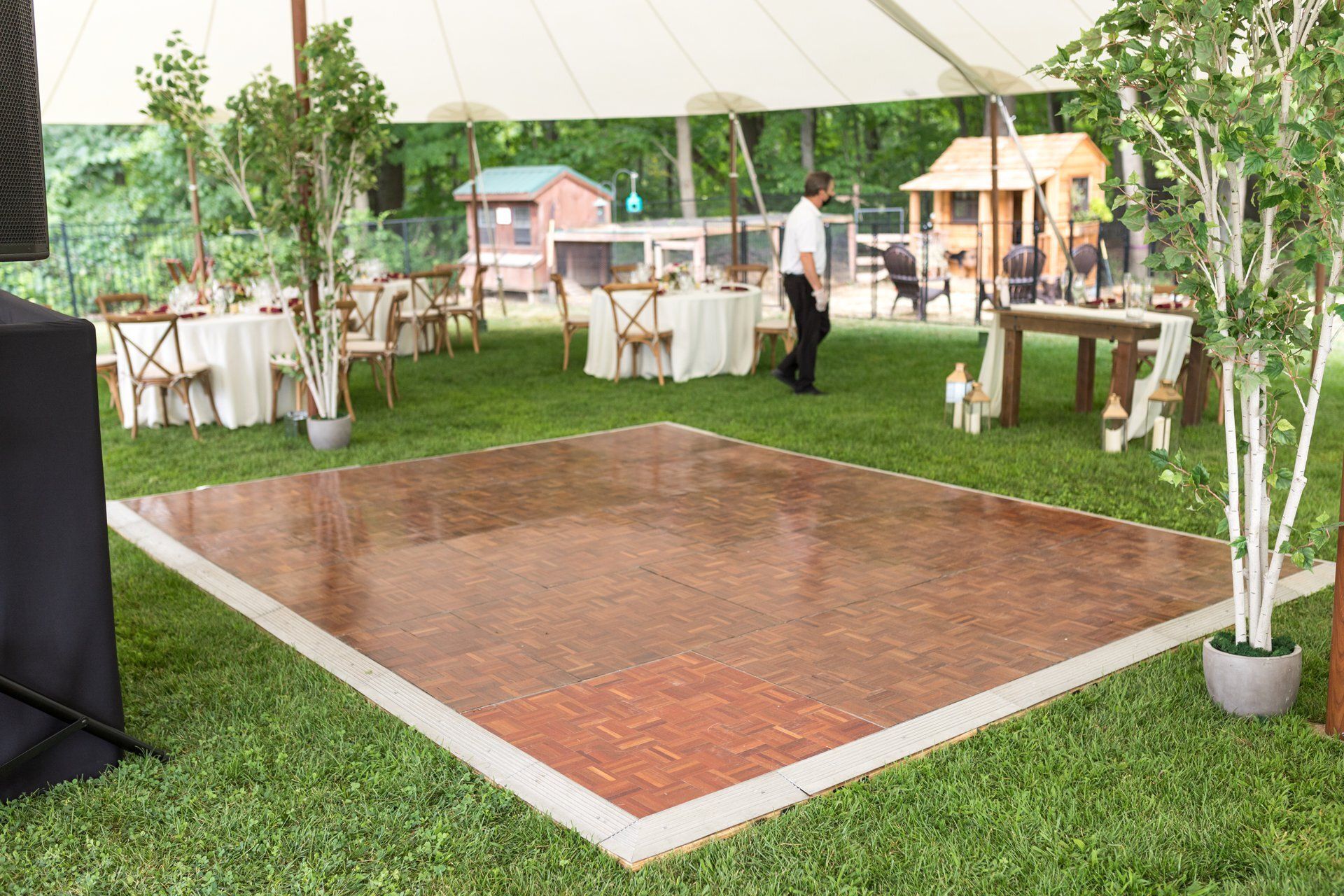 Empty dance floor under a white tent, with tables, chairs, and greenery at an outdoor event