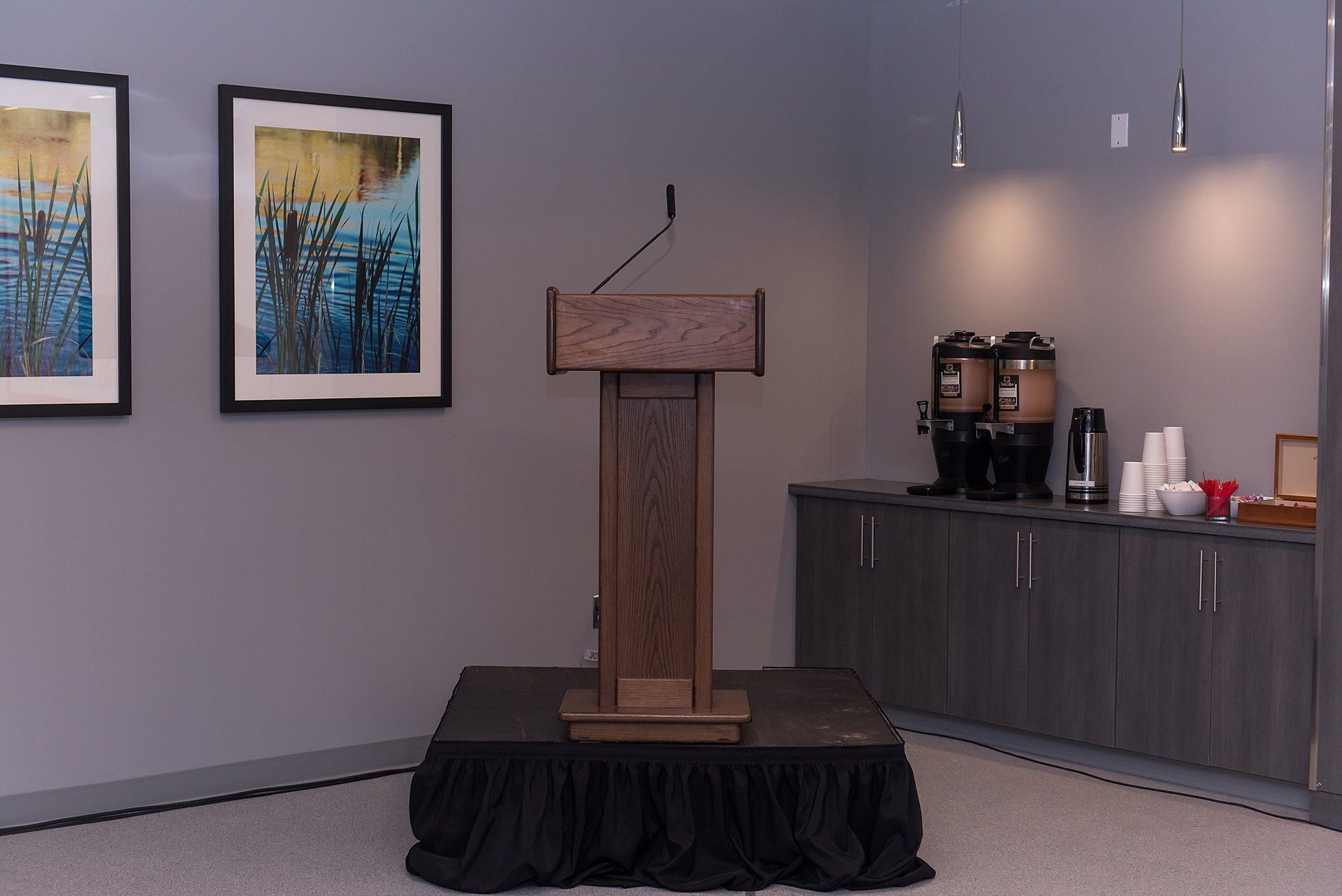 Podium on a black-draped platform in a reception room with framed art and a coffee station nearby