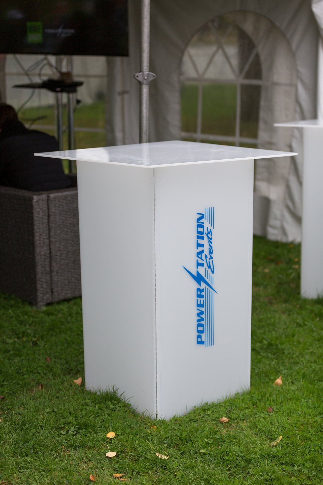 White podium stand on grass under a tent, with blue logo on the front.