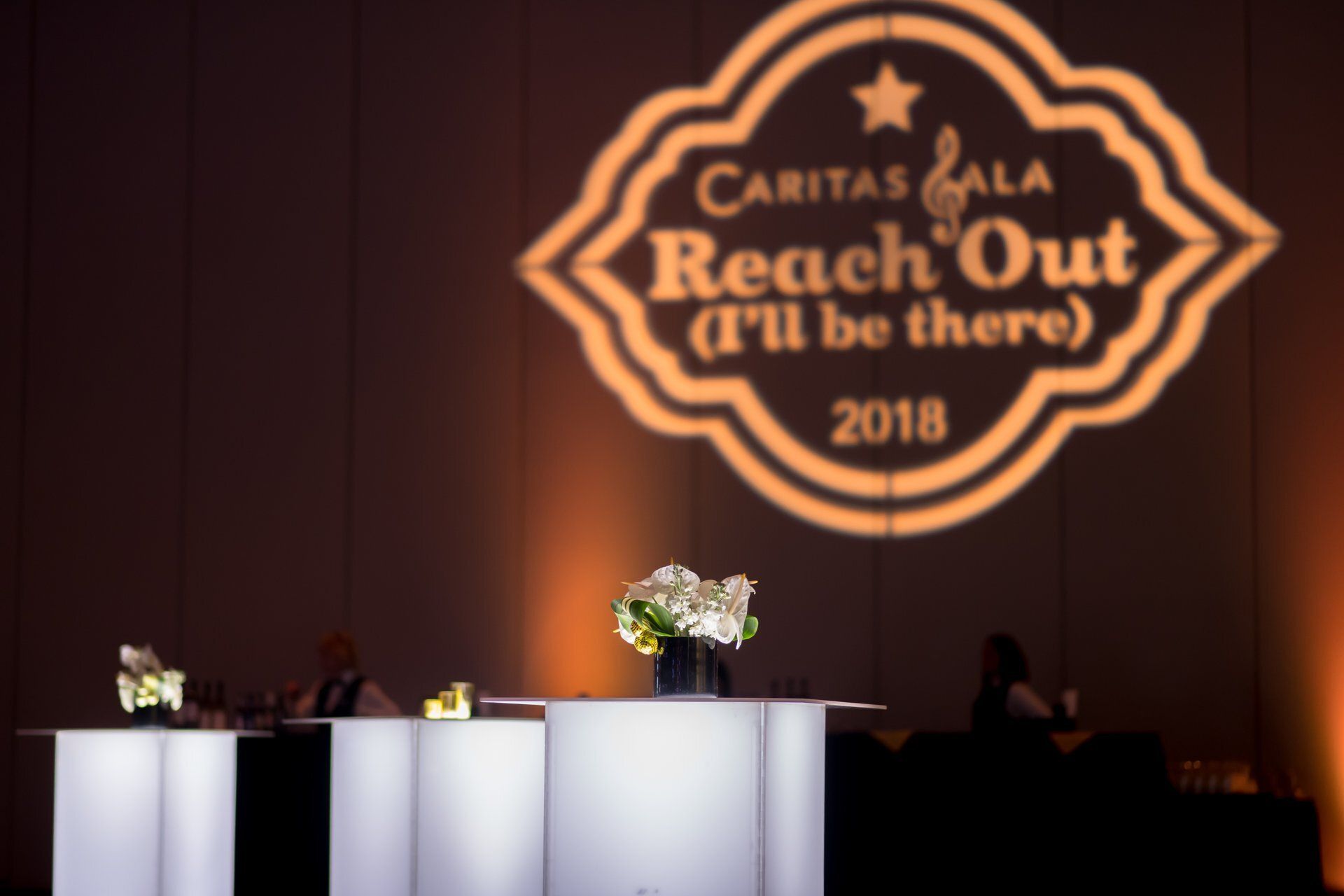 Stage with illuminated podiums and flowers beneath a “Reach Out” event logo on a dark backdrop.