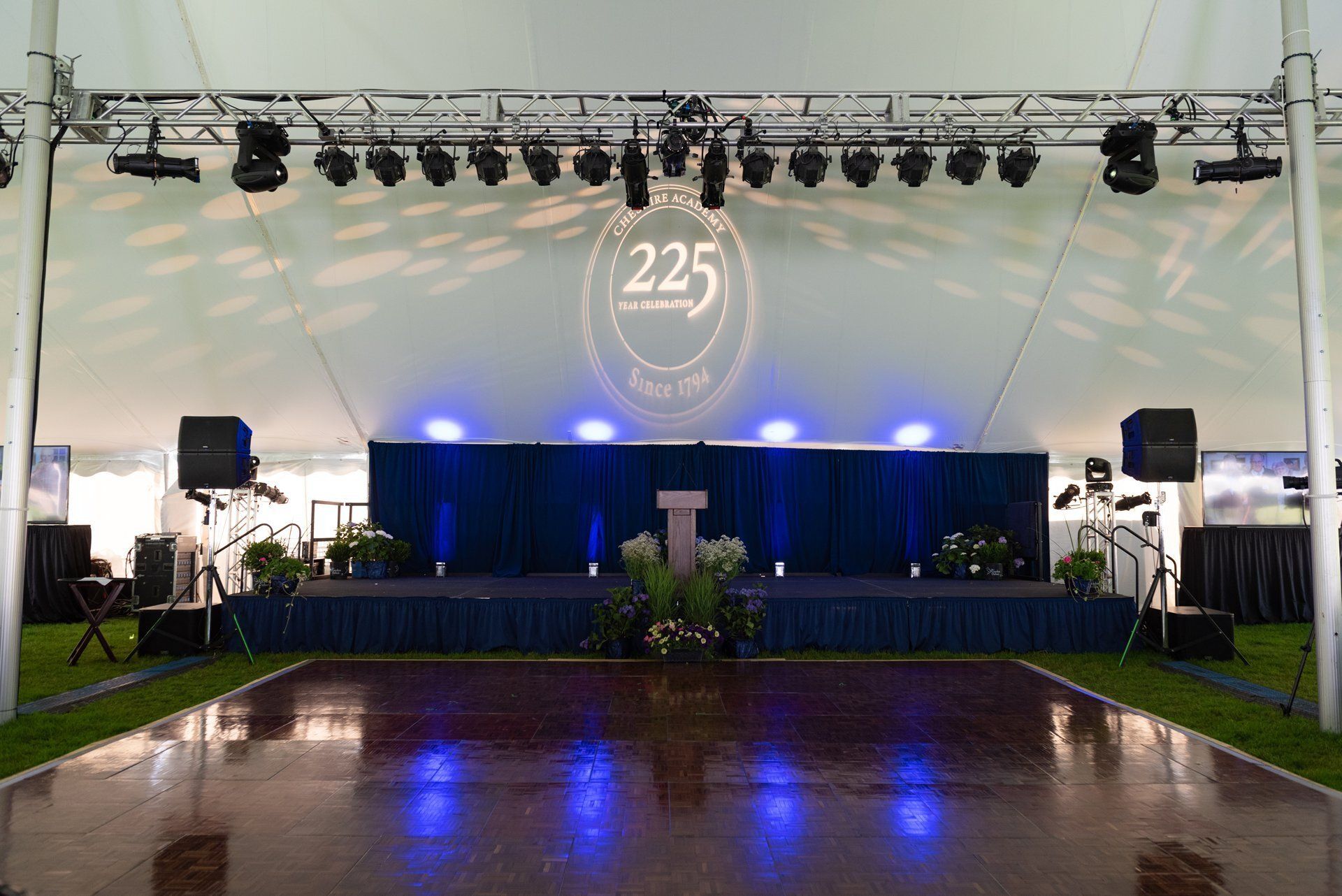 Empty event stage under a white tent with blue lights and a wet reflective floor, marked with a “225” sign