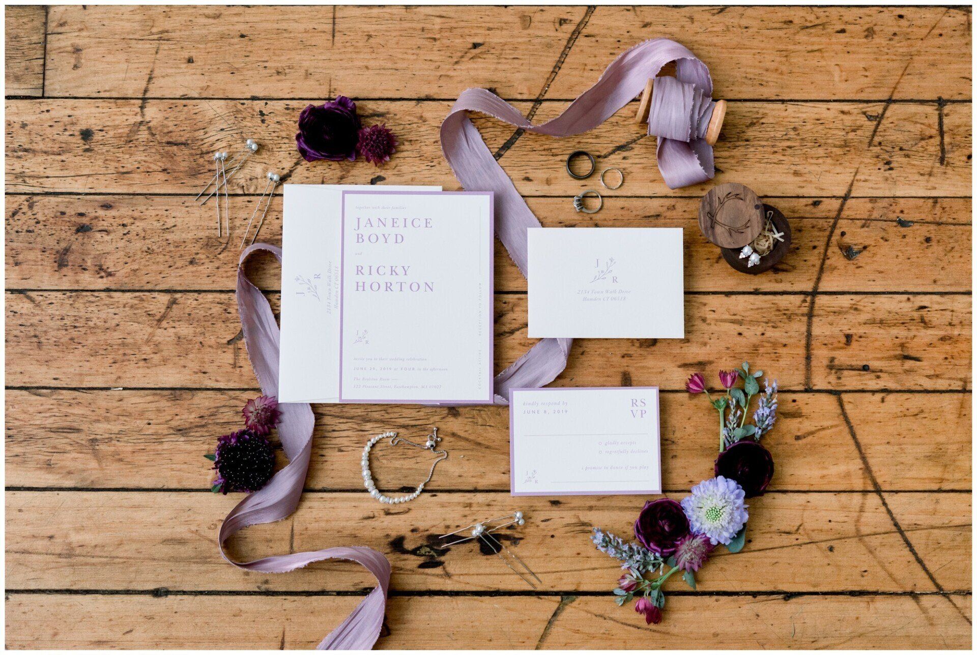 Wedding stationery flat lay on rustic wood with lavender ribbons and floral accents