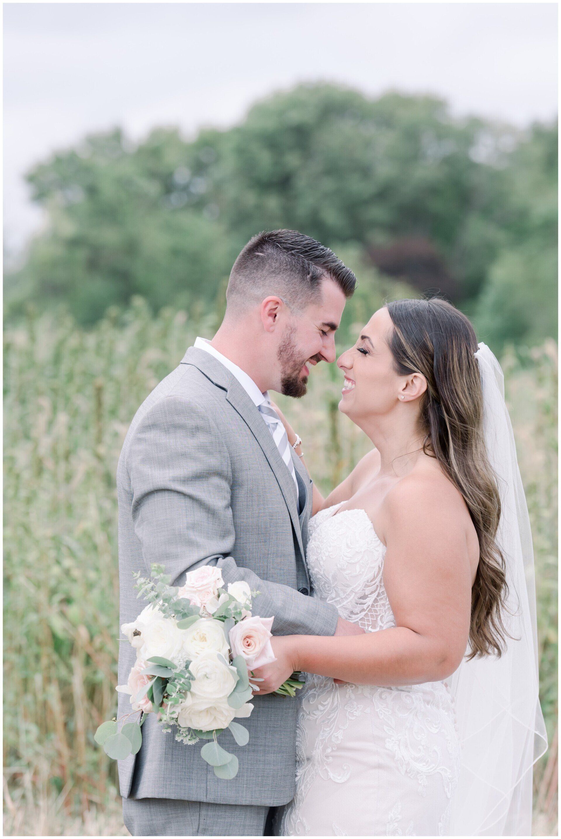 Bride and groom embracing outdoors, with bouquet and veil in soft green setting