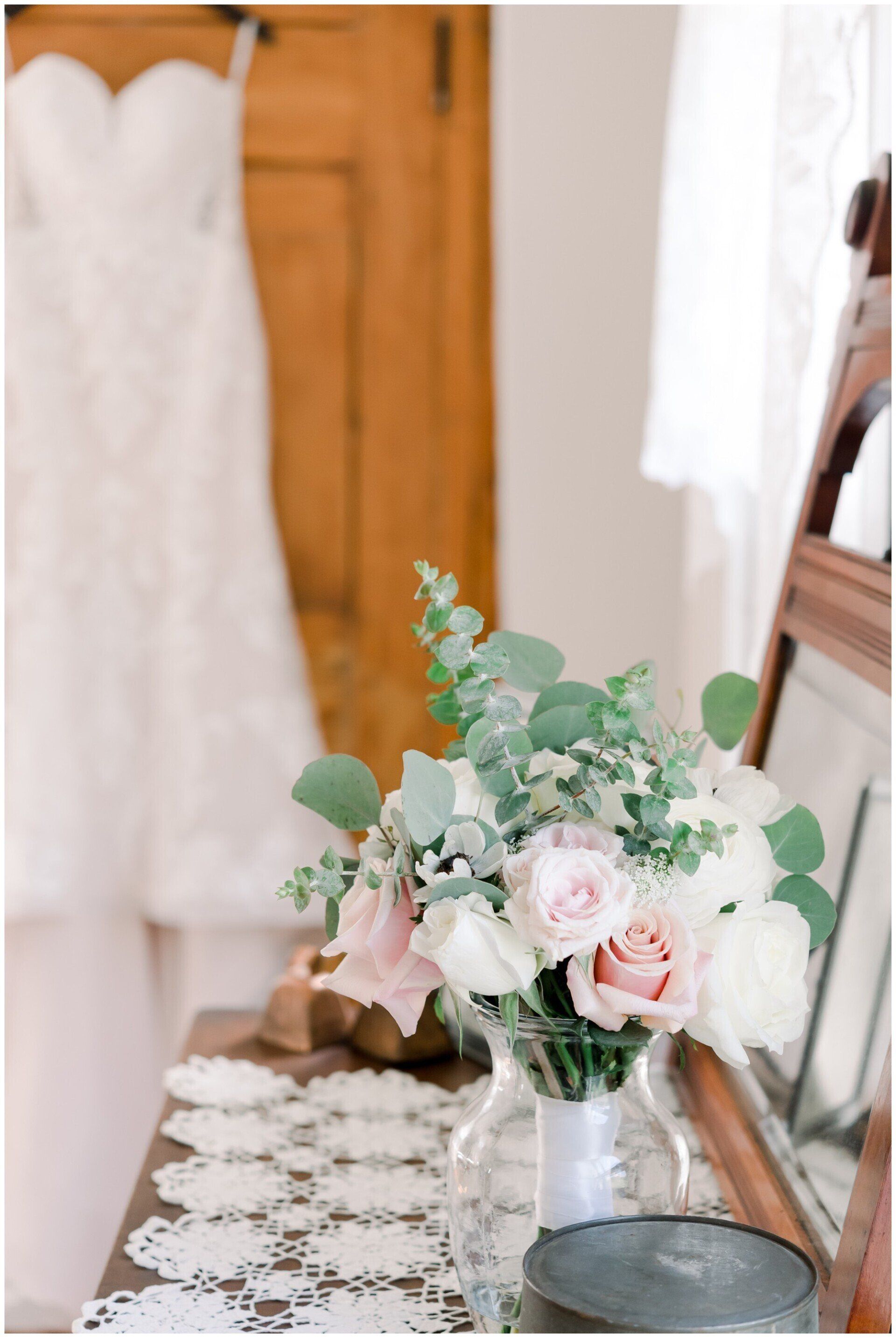 Bridal bouquet on a lace-covered table beside a white wedding dress and mirror