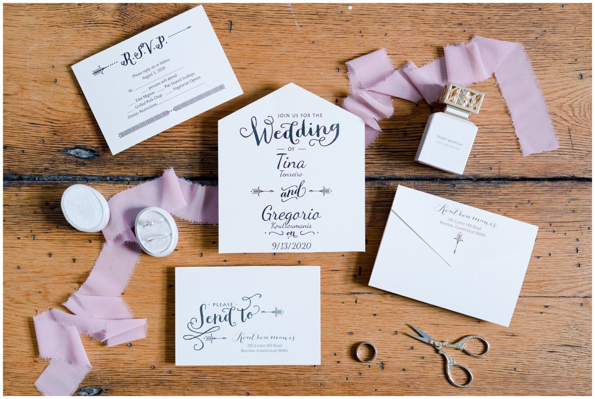 Wedding stationery suite on wooden table with lavender ribbon, envelopes, cards, wax seal, and scissors
