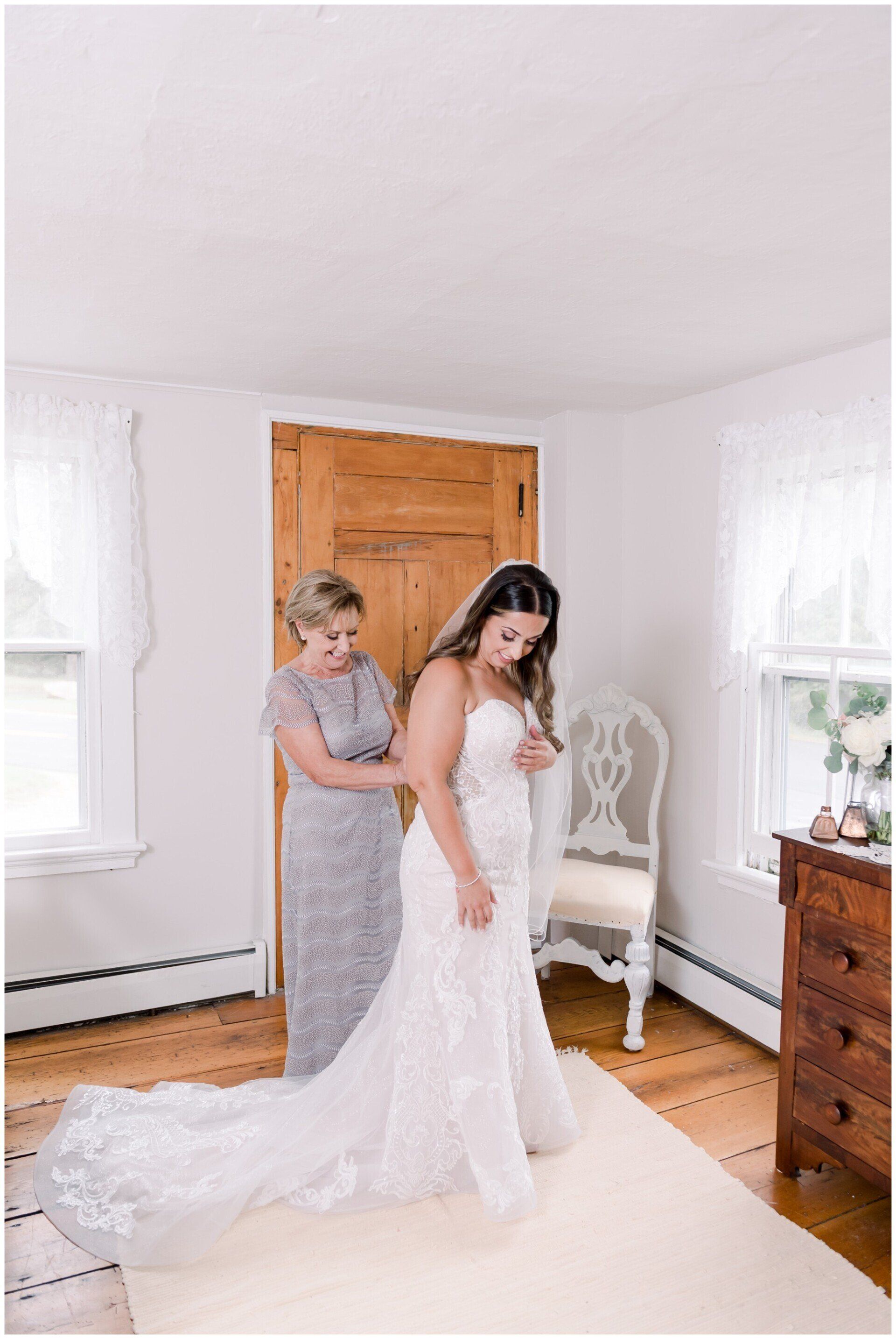 Bride being helped into a white wedding dress in a bright room with wooden doors and white furniture