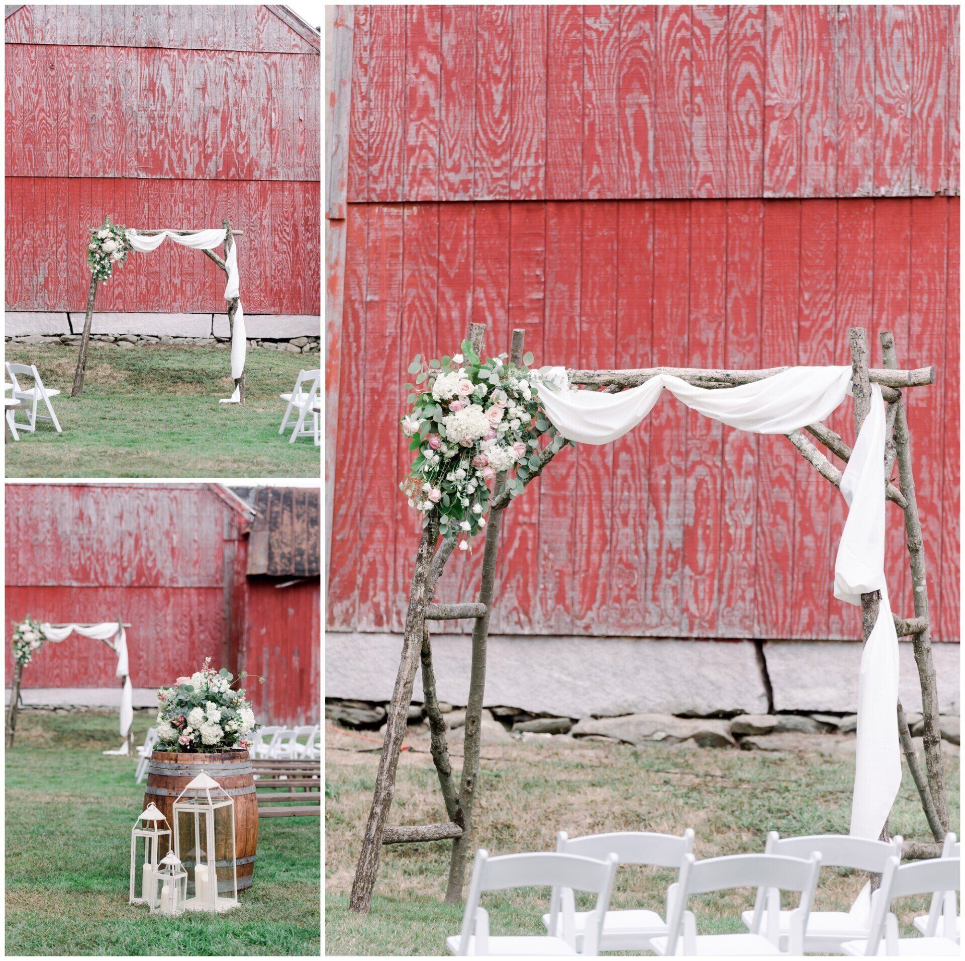 Rustic wedding arch with white draping and flowers against a weathered red barn, with white chairs in front