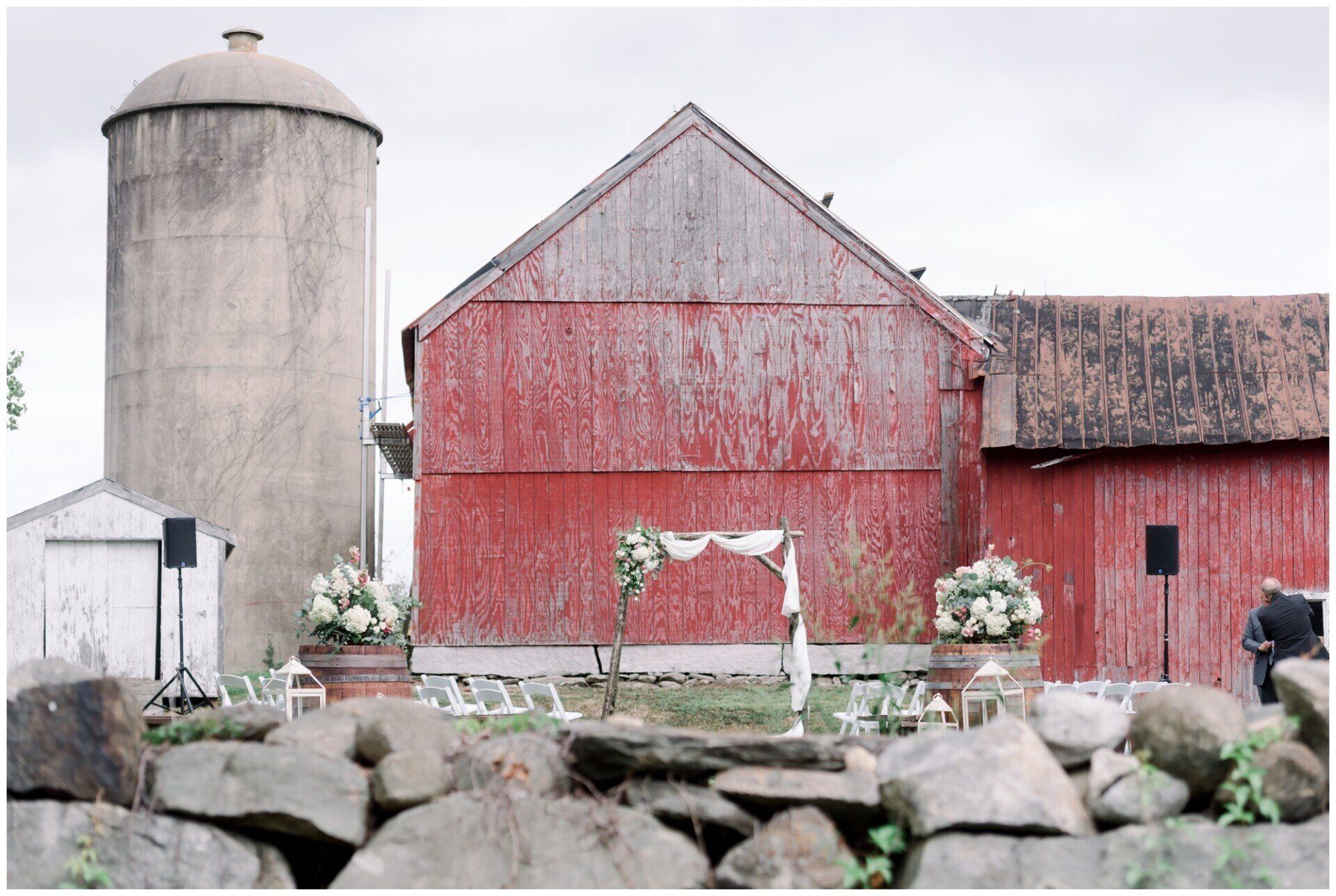 Red barn and silo behind a stone wall, with white flowers in front
