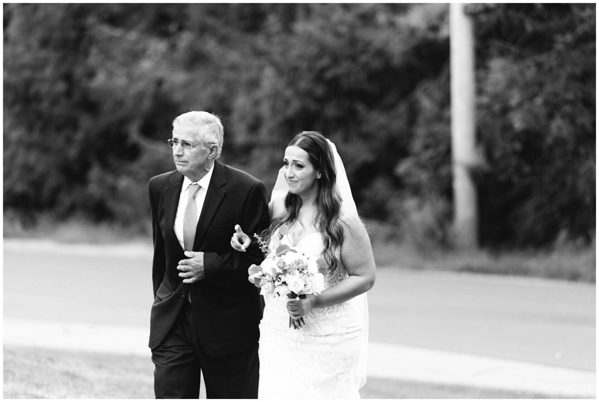 Bride and older man walking outdoors, bride holding a bouquet and both in formal attire