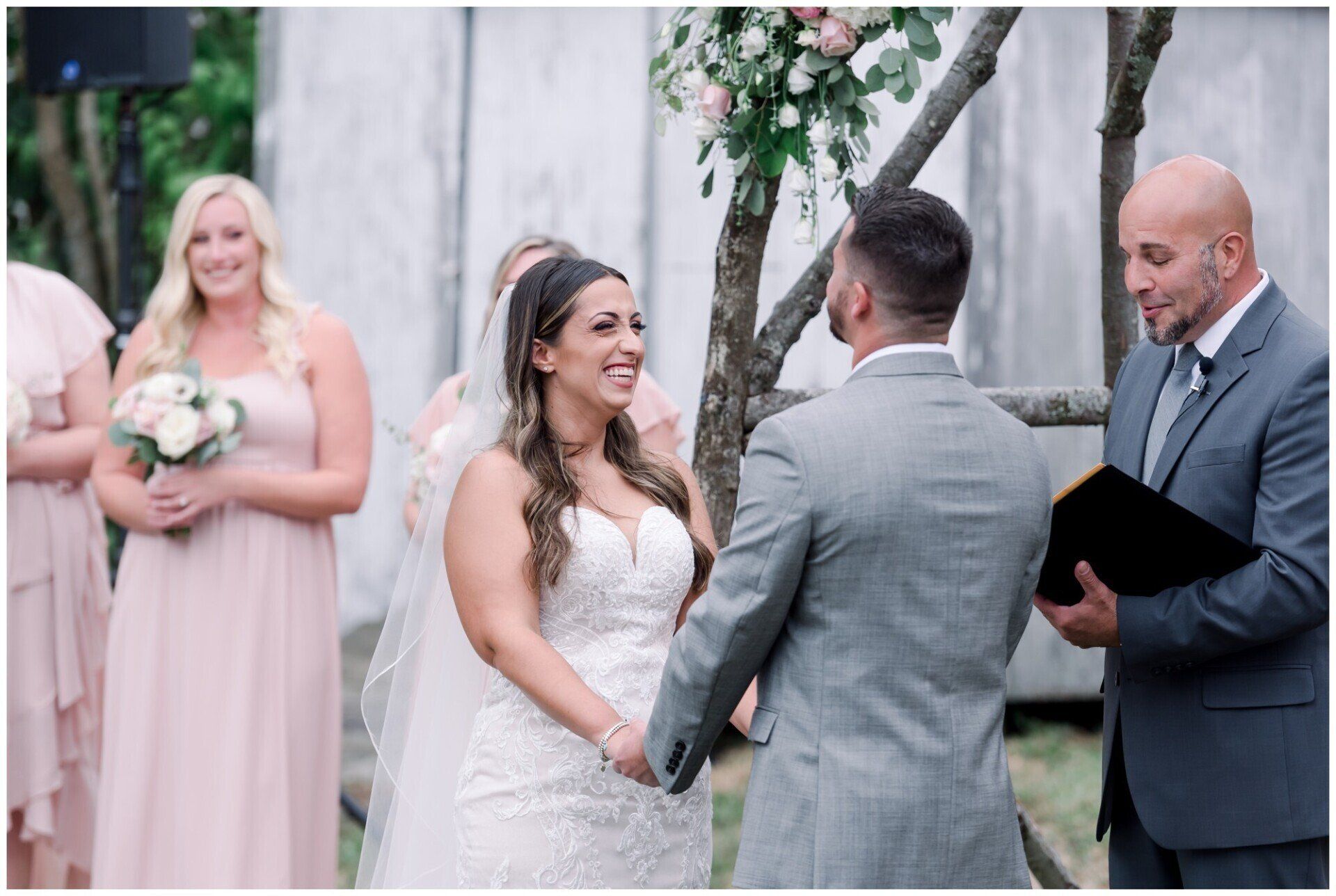 Bride and groom exchange vows at an outdoor wedding ceremony, smiling before a floral arch.