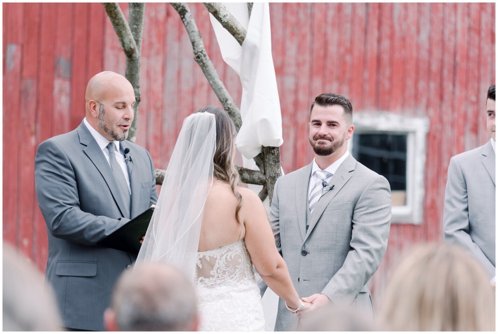 Bride and groom exchange vows at an outdoor wedding ceremony before a red barn.