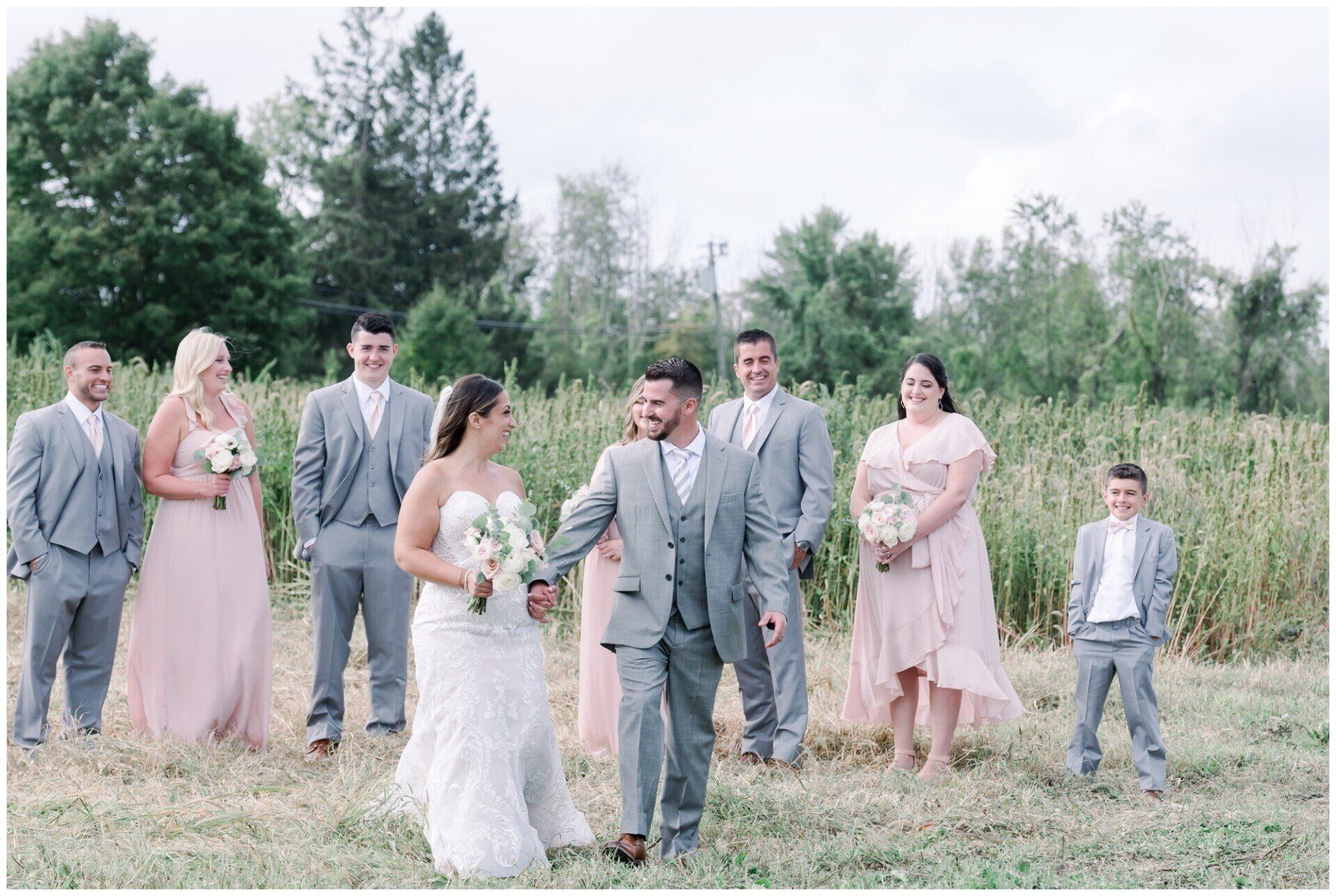 Wedding party walking in a grassy field with trees in the background