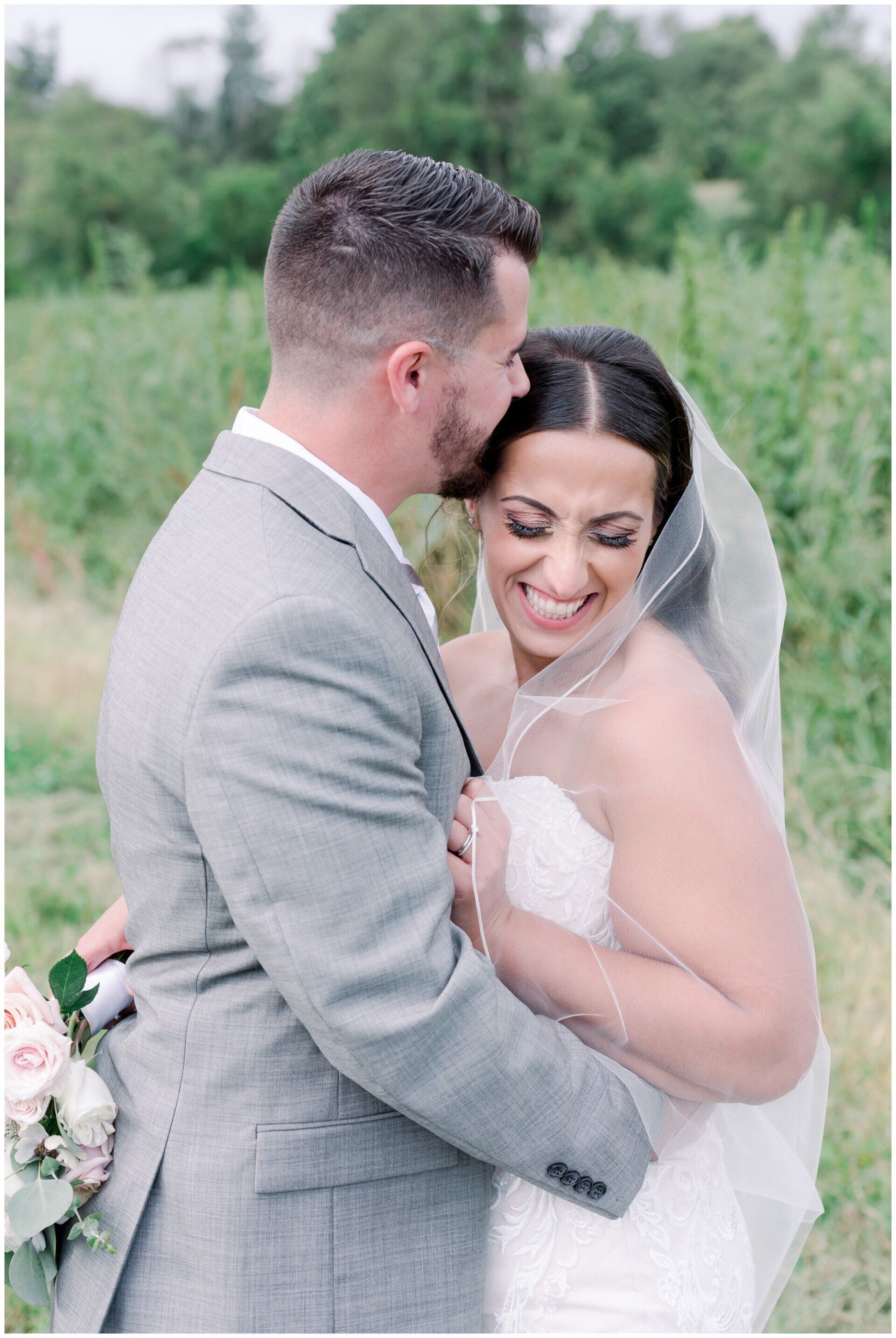 Bride and groom embrace outdoors, smiling in a soft-focus garden setting