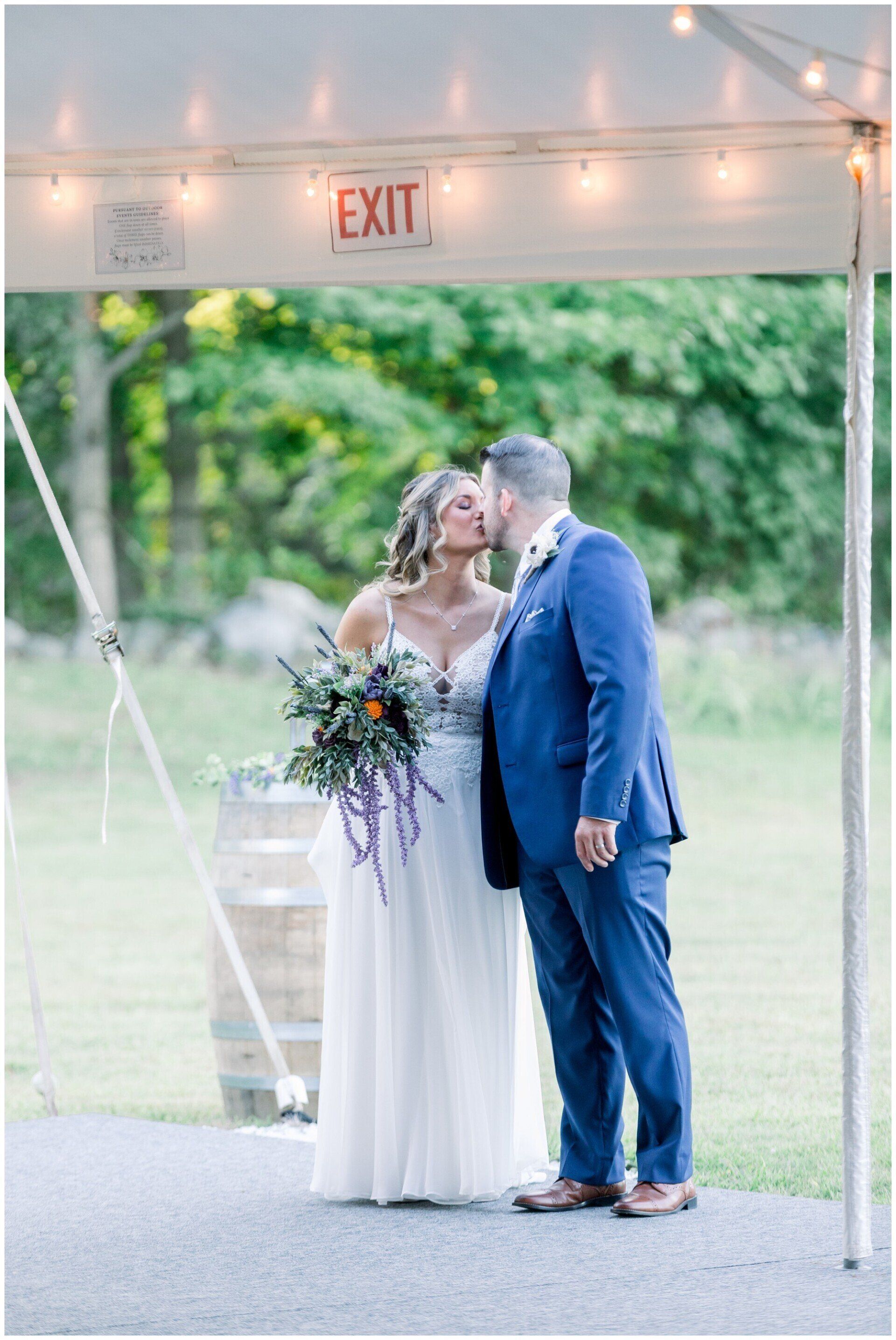 Bride and groom kissing under a tent at an outdoor wedding ceremony