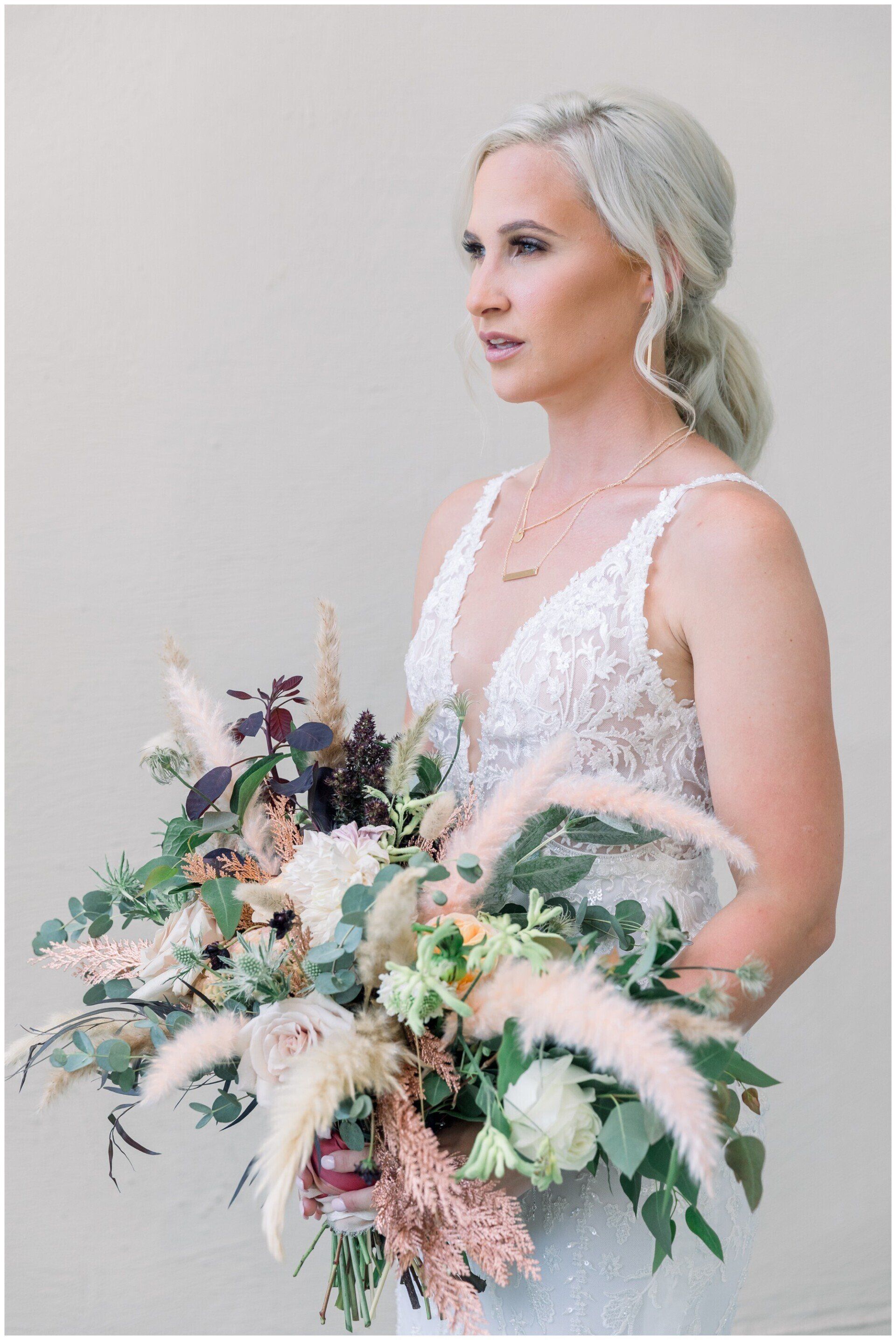 Woman in a white dress holding a large pastel floral bouquet against a light gray wall
