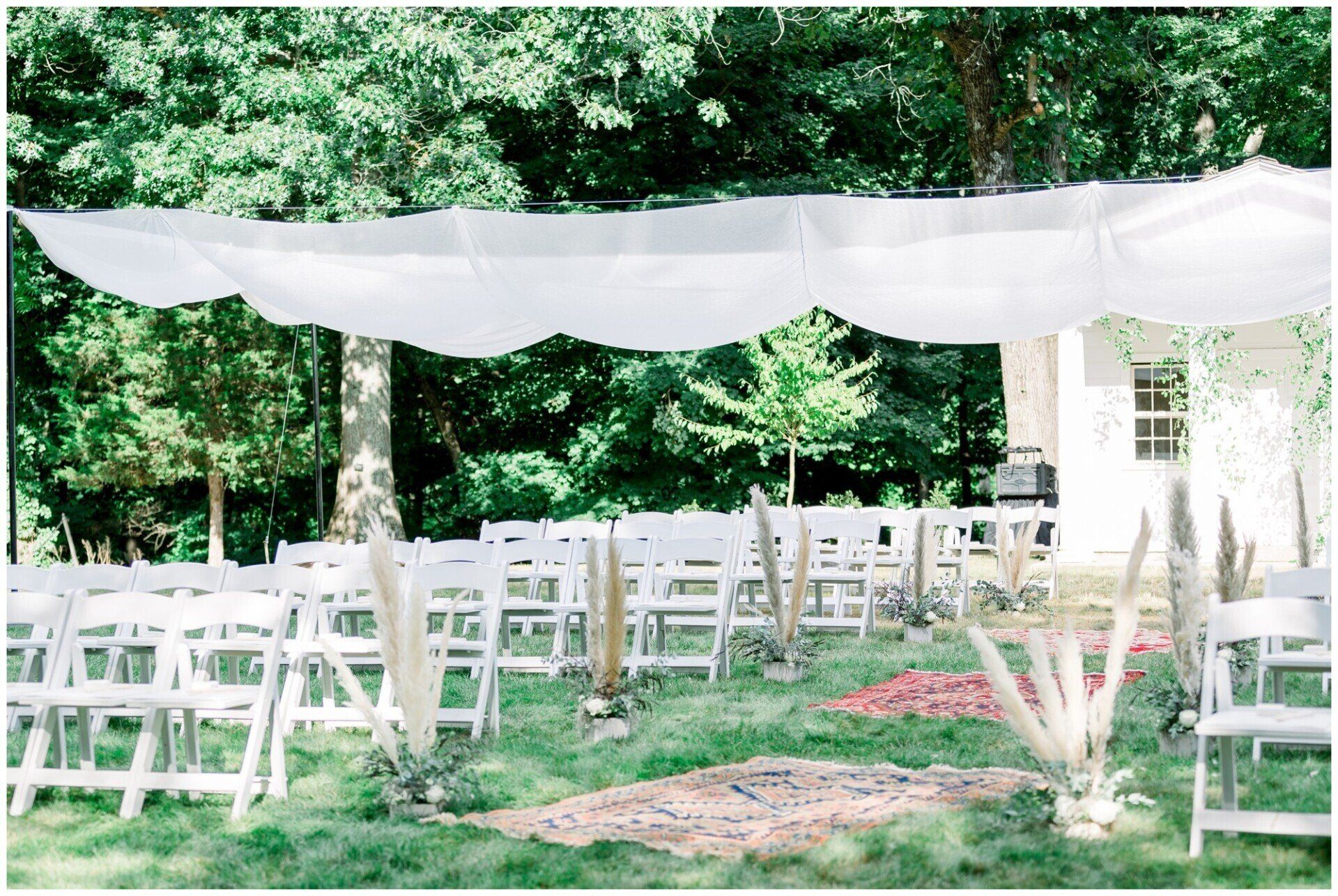 White outdoor wedding tent with rows of chairs on a grassy lawn surrounded by trees