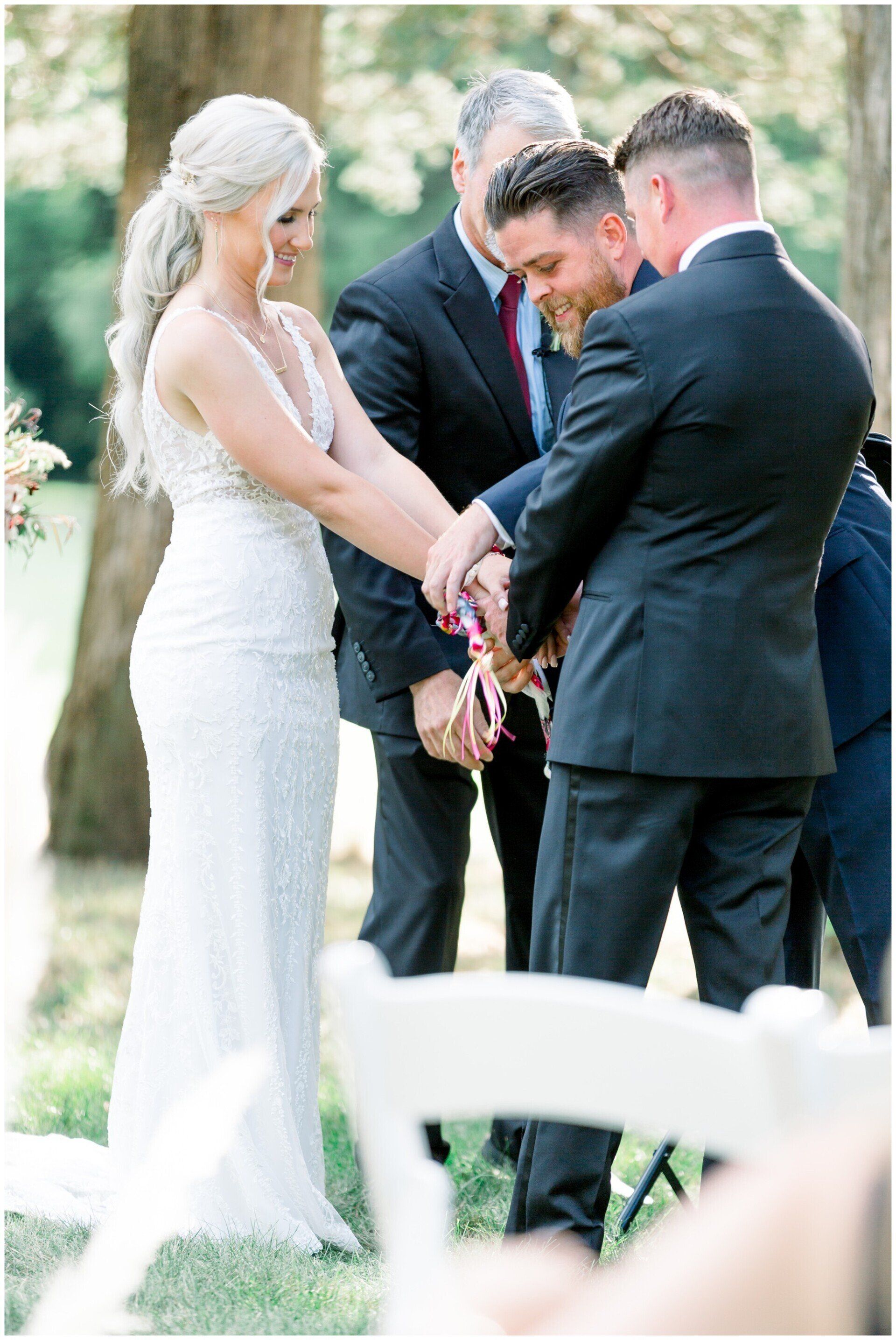 Wedding party joining hands during an outdoor ceremony on a grassy lawn