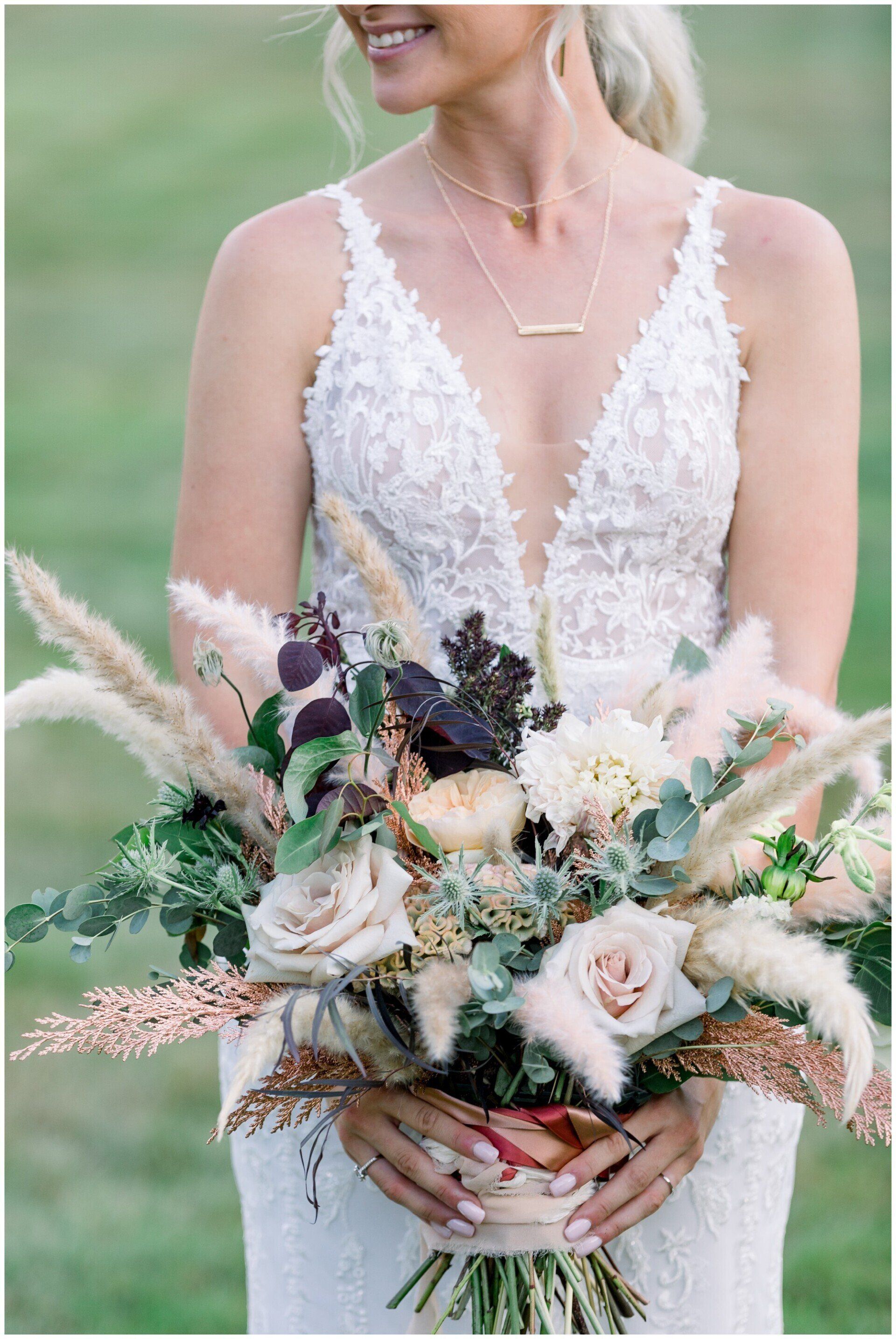 Bride in a lace dress holding a pastel wildflower bouquet outdoors