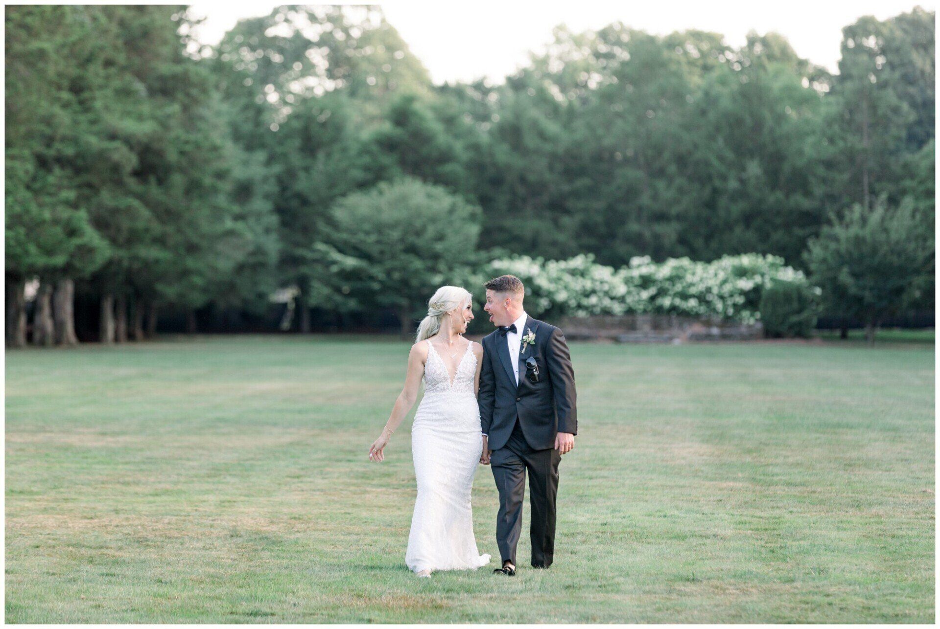 Bride and groom standing on a grassy lawn with trees in the background