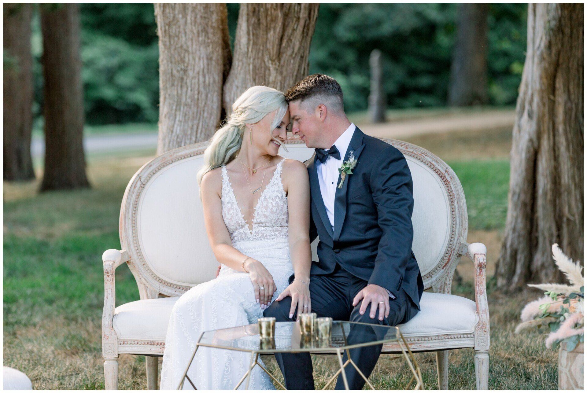 Wedding couple sharing a kiss on a vintage white loveseat outdoors among trees