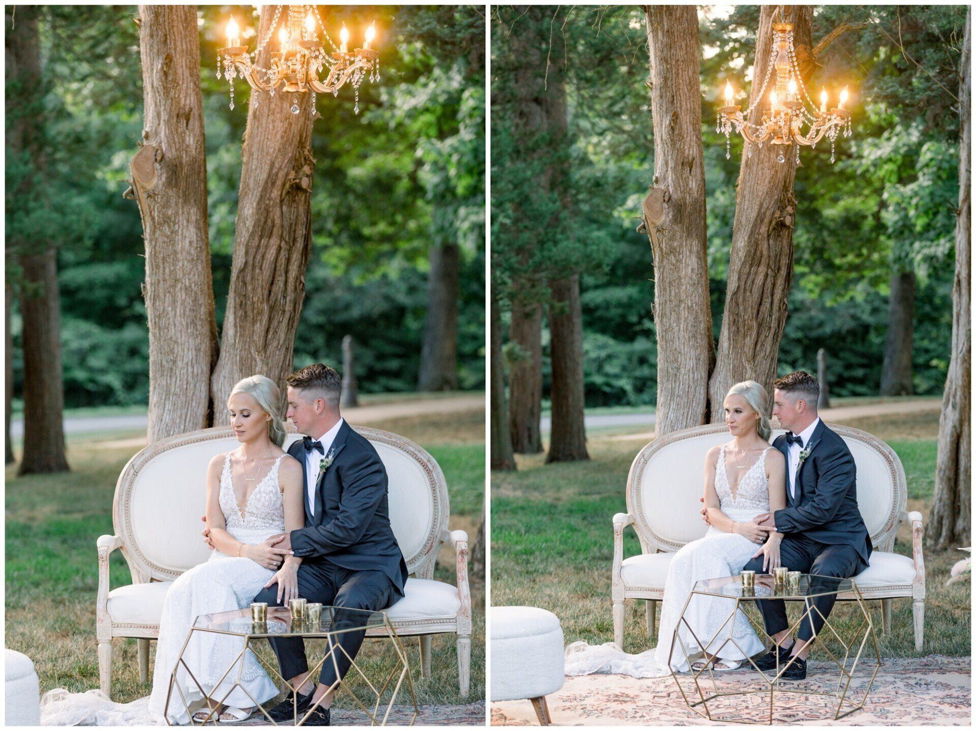 Bride and groom seated on a white loveseat under a chandelier in a wooded outdoor setting