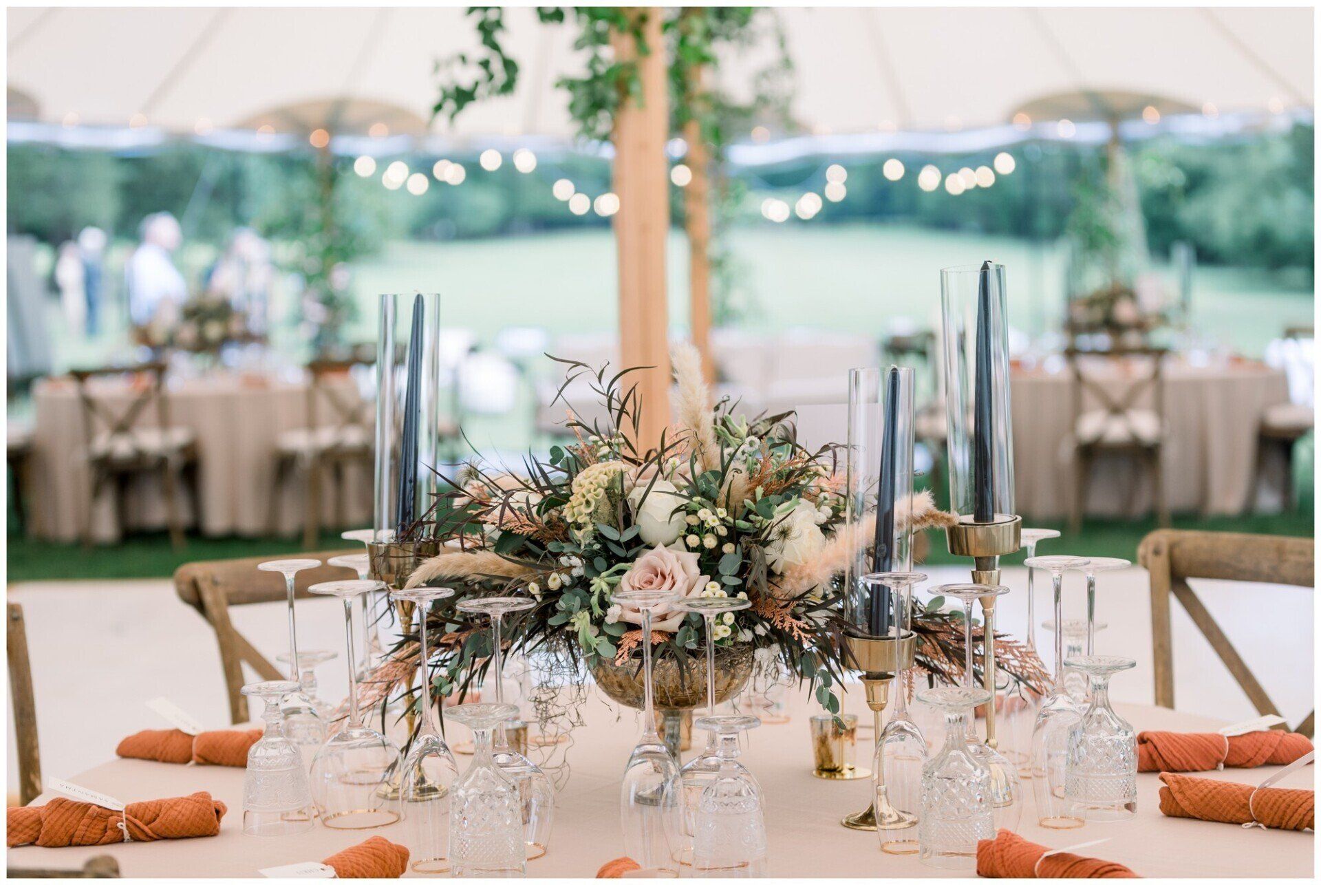 Elegant outdoor wedding reception table with floral centerpiece, glassware, candles, and white canopy in a garden setting