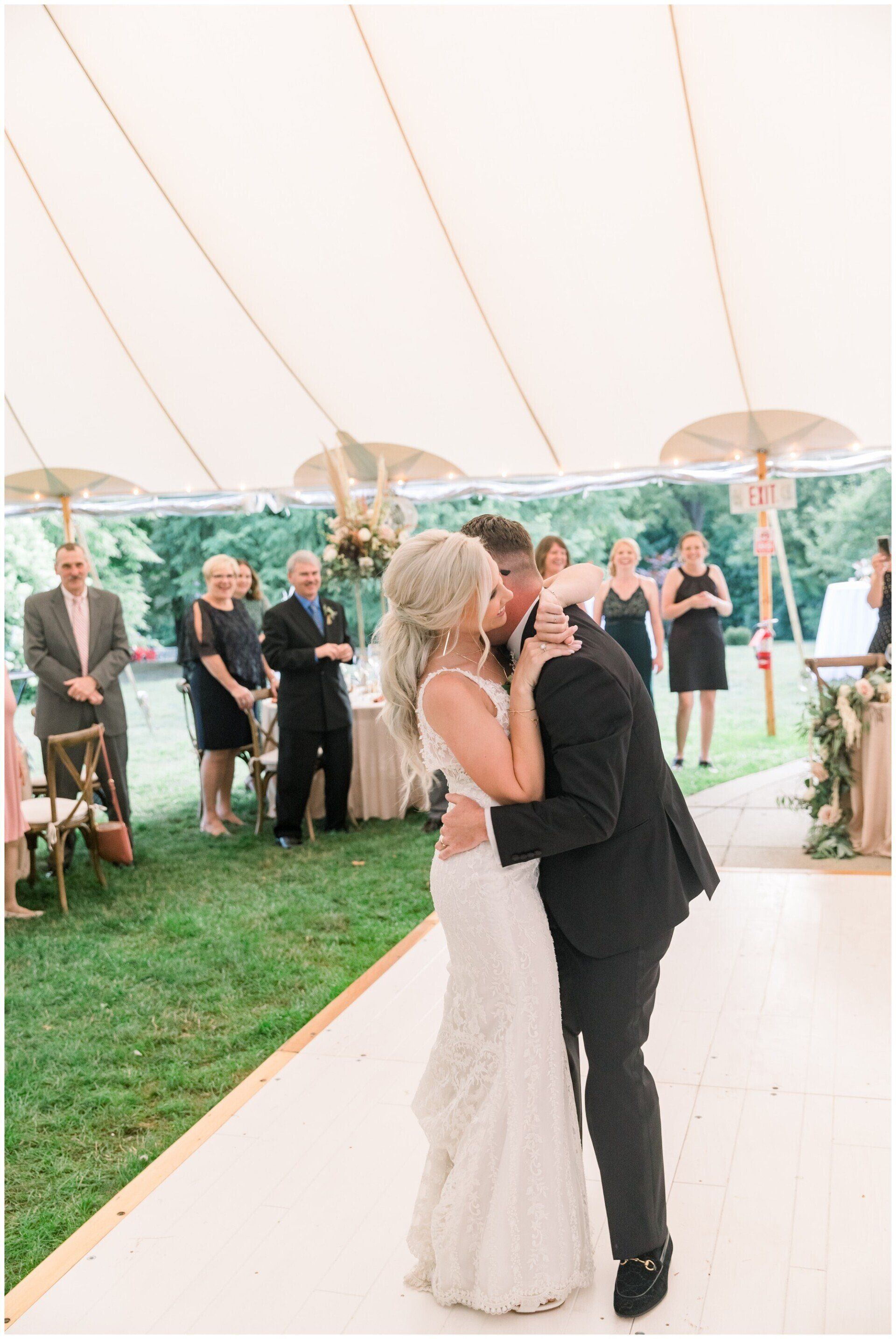 Bride in white dress and groom in black suit kissing under a tent at a wedding reception